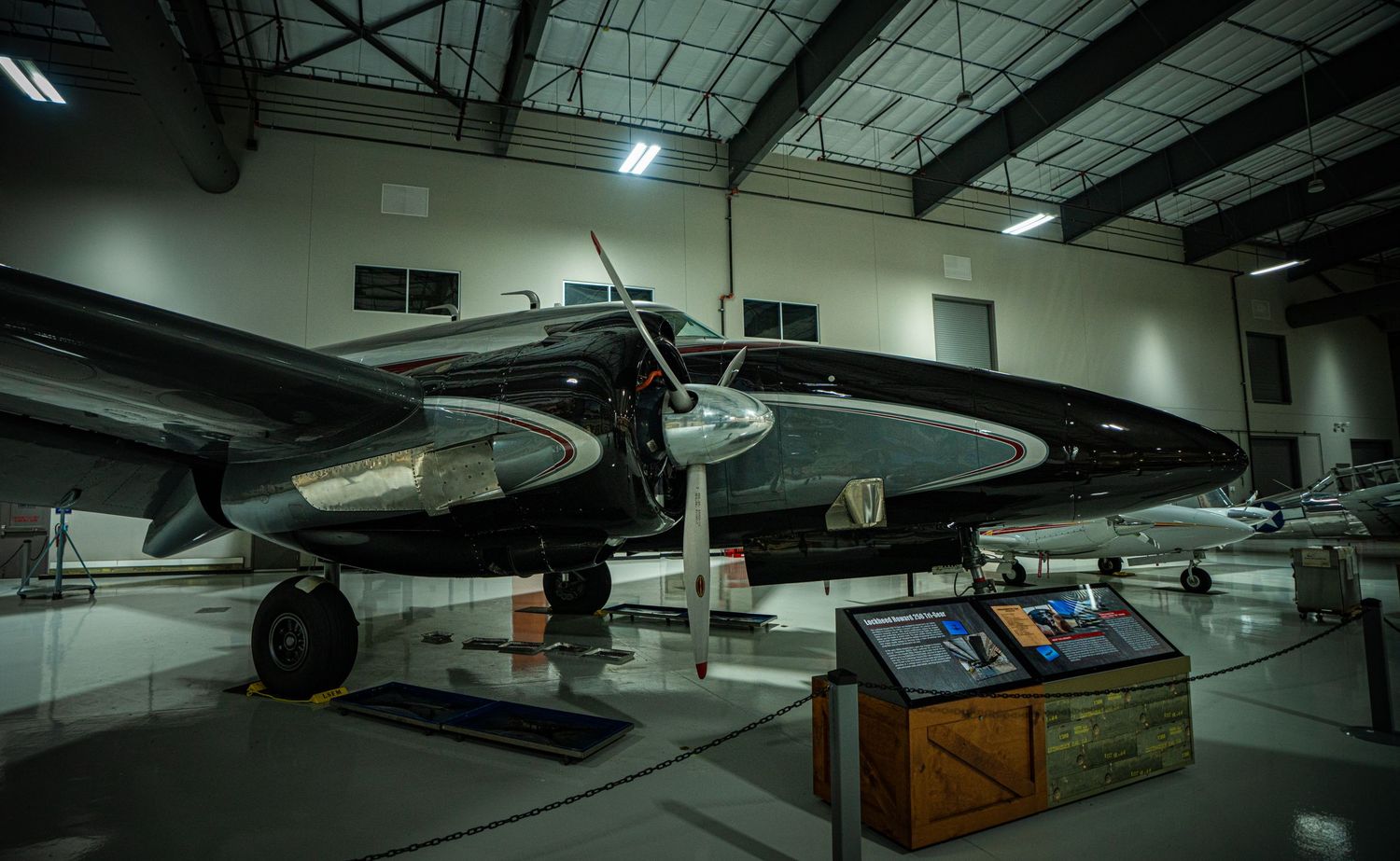 Vintage twin-engine aircraft on display inside a museum hangar with informational placard nearby.