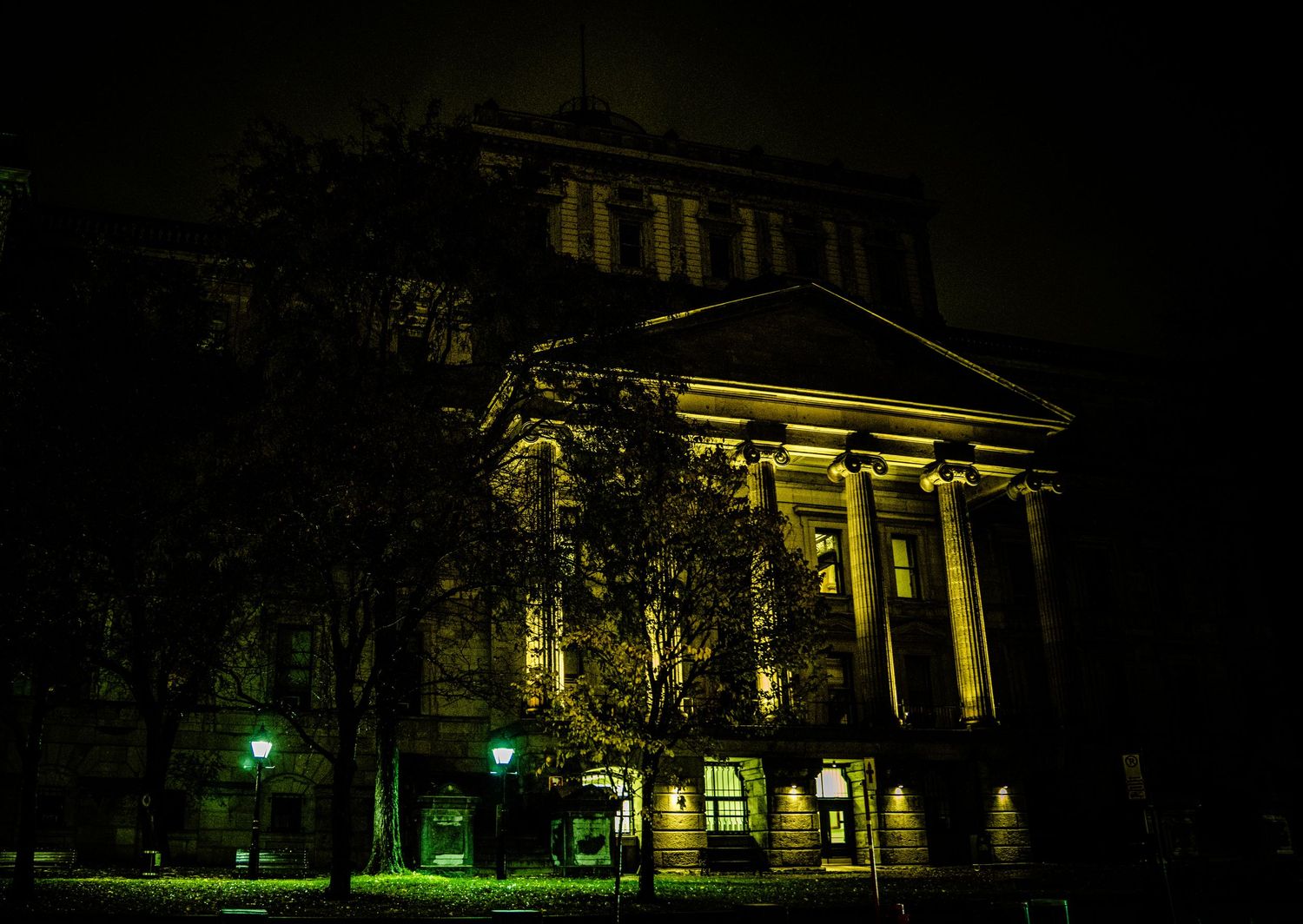 A series of illuminated historic buildings and columns at night with dramatic yellow lighting and dark shadows.