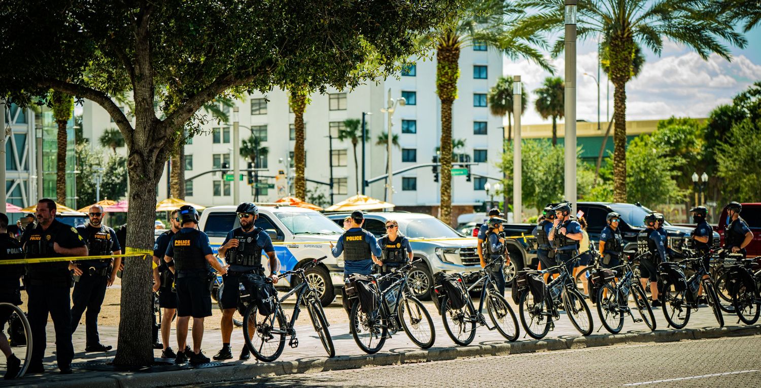 Row of police officers on bicycles line up along a street barrier.