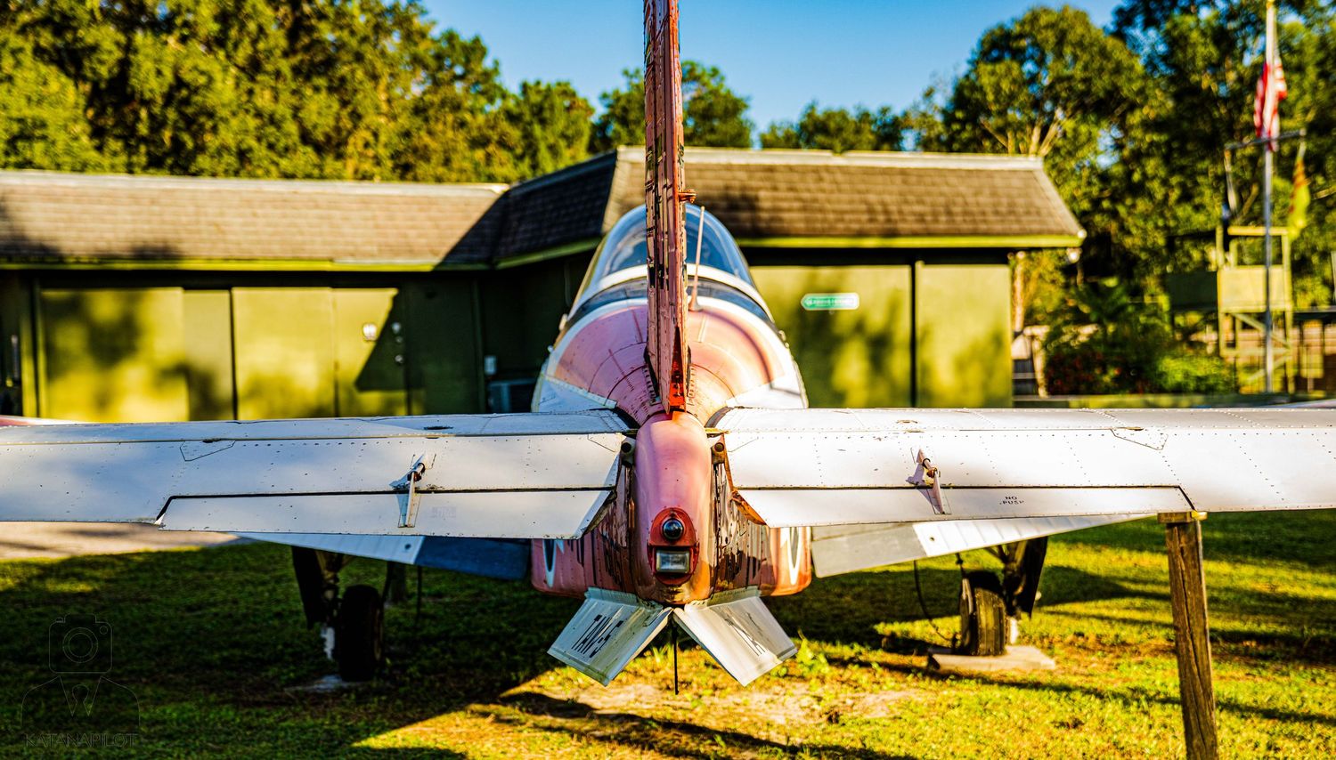 Vintage aircraft parked on grass field under bright blue sky with trees in background.