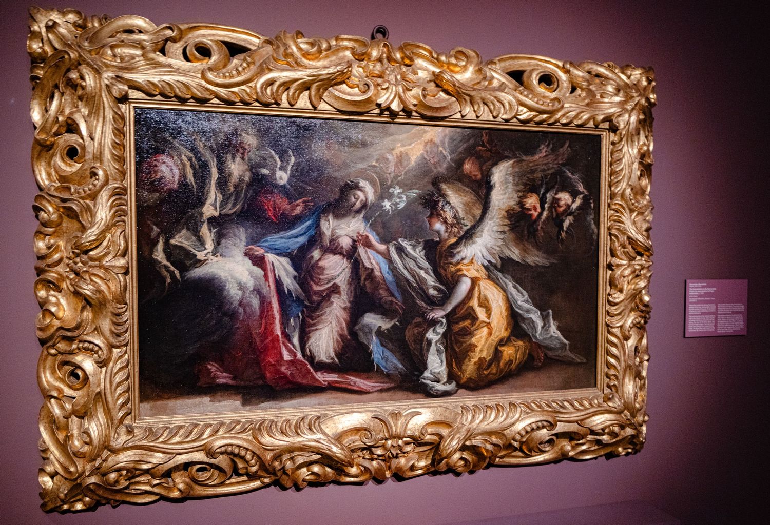 Baroque painting in ornate gold frame displayed on pink wall in art museum gallery.