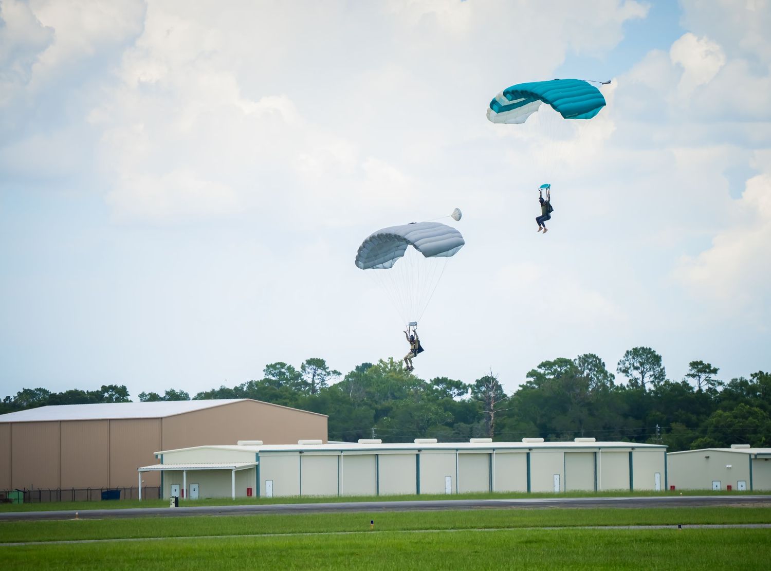 Sequence of a skydiver landing with a blue parachute on a grassy field near industrial buildings.