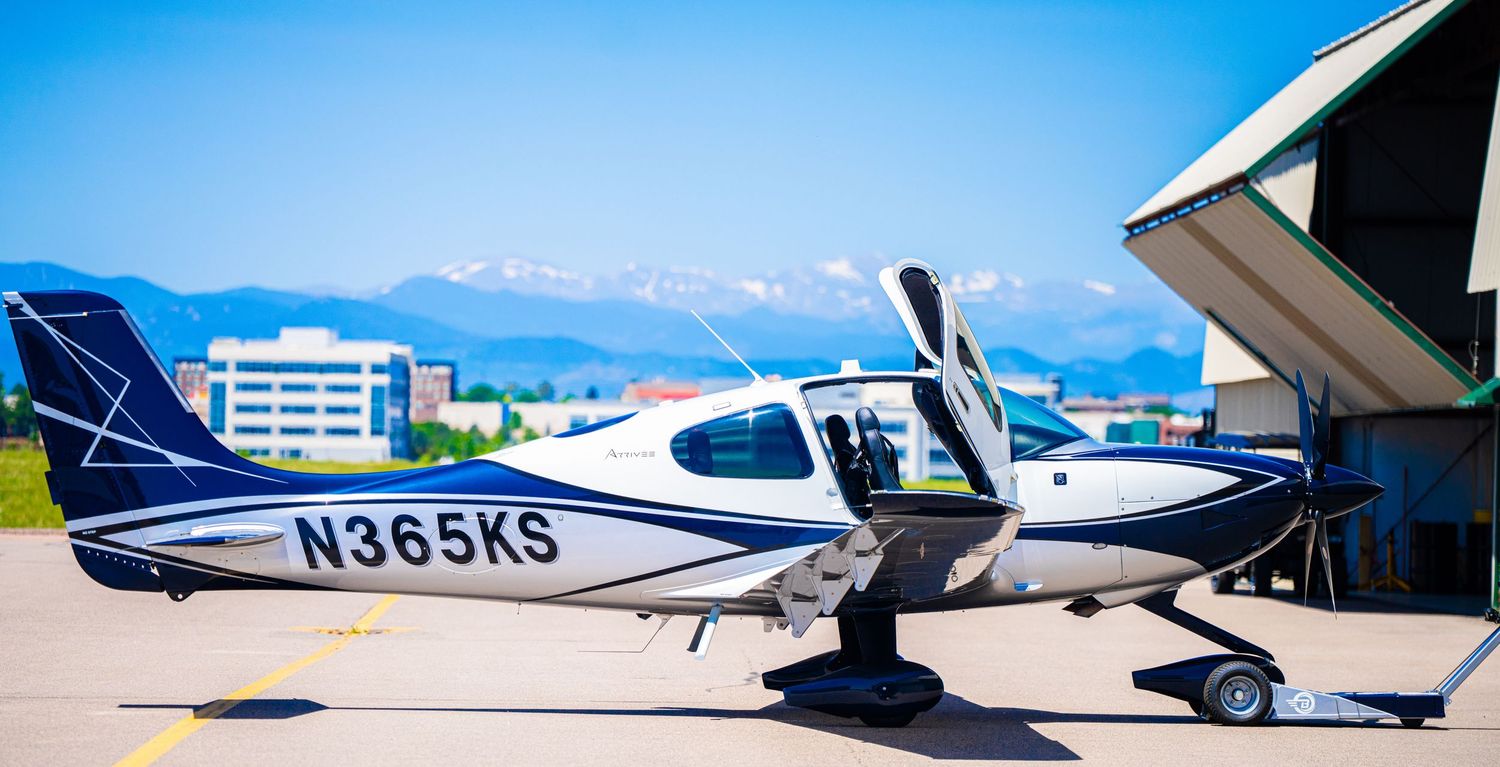 Row of small private aircraft parked on tarmac under bright blue sky.