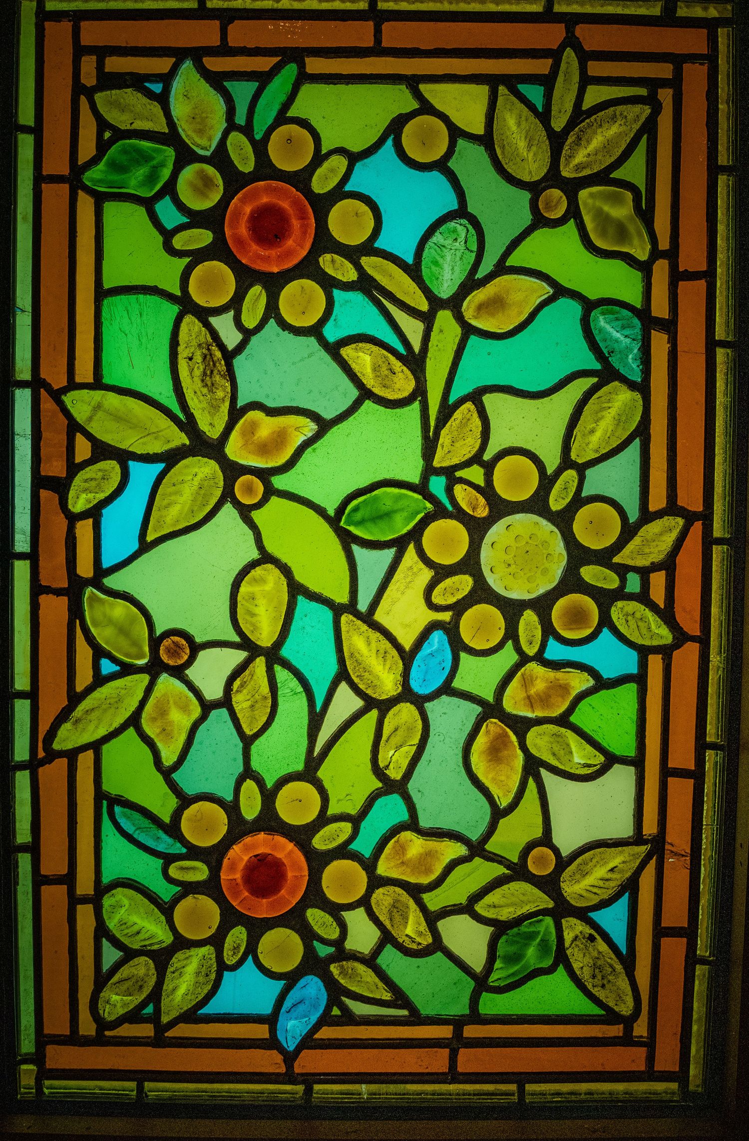 Decorative stained glass window featuring yellow sunflowers and green leaves in a geometric pattern.
