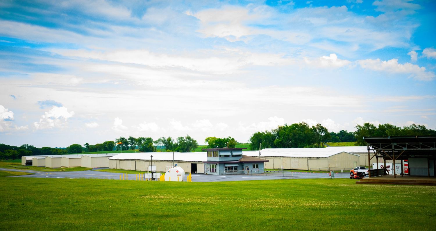 Rural airport facility with hangars and runway visible under bright blue skies.
