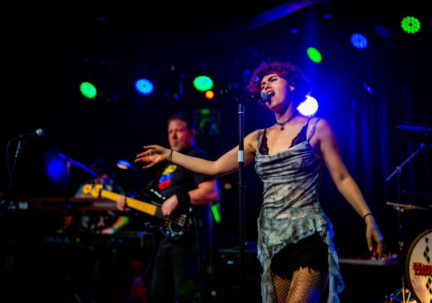 Female singer performing on stage with band members and colorful lights at a live music concert venue.