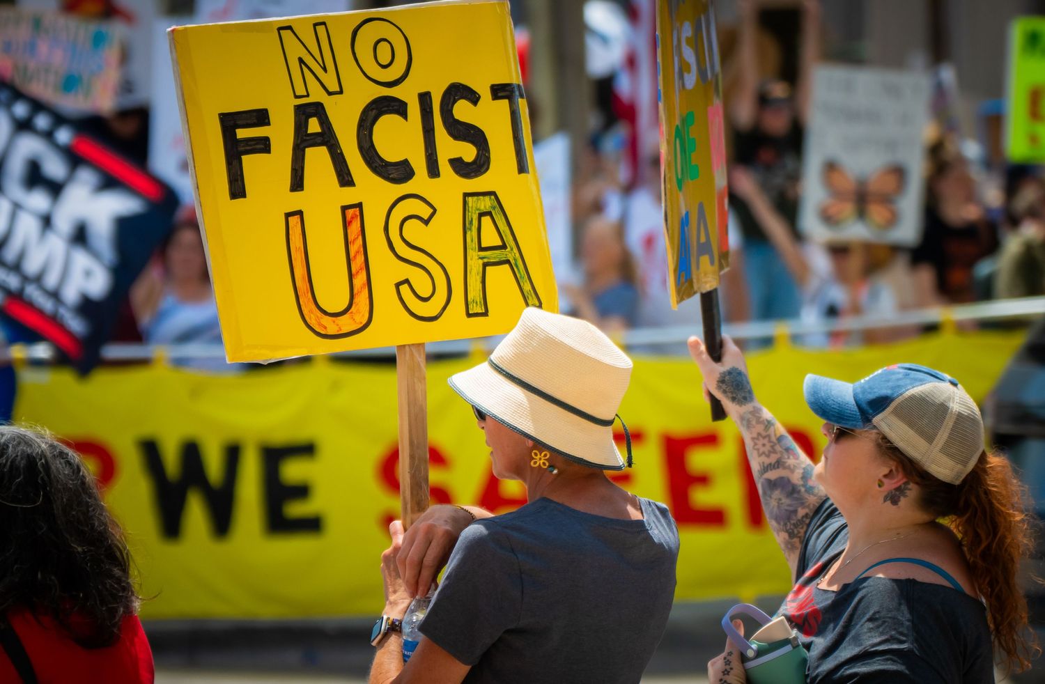 Protesters hold yellow anti-fascist sign during political demonstration with crowd visible in background.