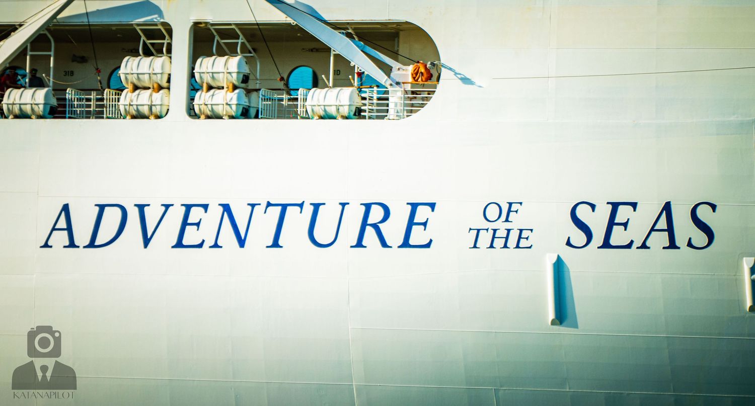 The name 'Adventure of the Seas' written in blue text on the white hull of a cruise ship.