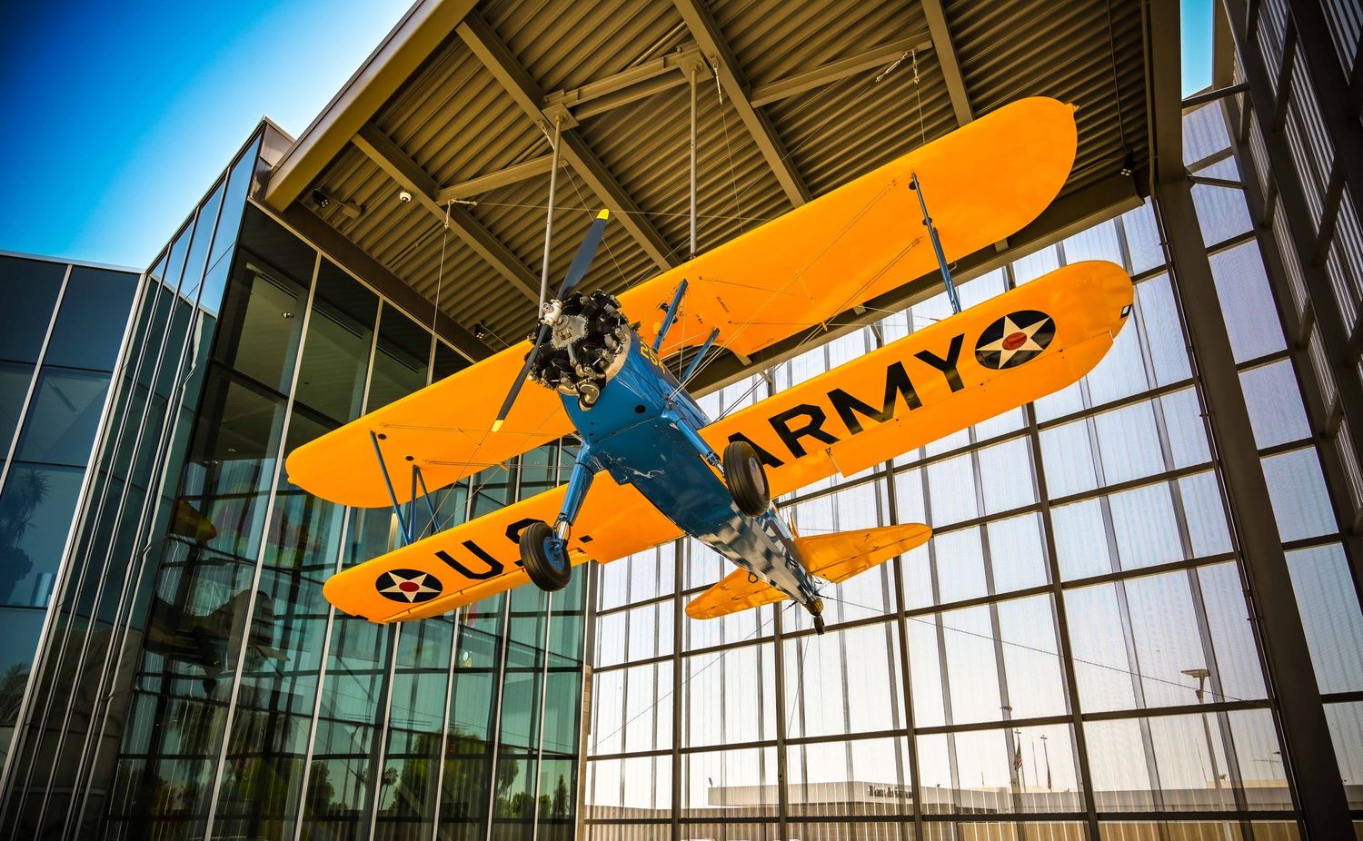 Vintage yellow airplane displayed in modern museum with glass ceiling and architectural details.