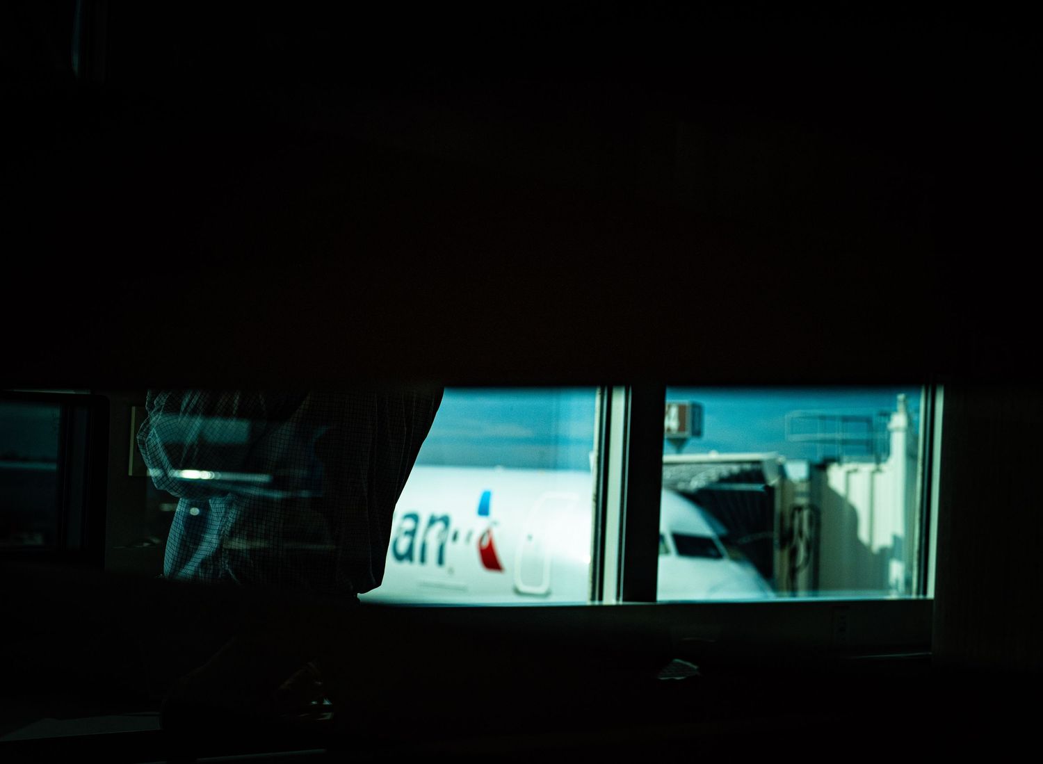 A dimly lit window illuminated in blue light reveals a partial view of a commercial sign at night.