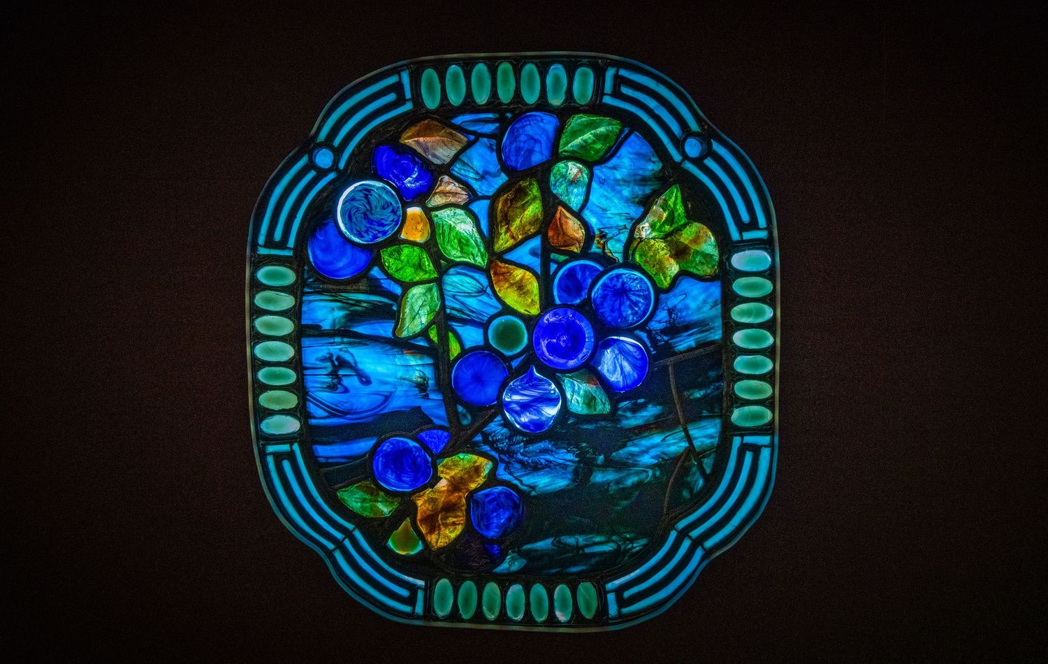 Circular stained glass design featuring blue and green floral patterns in an ornate border.
