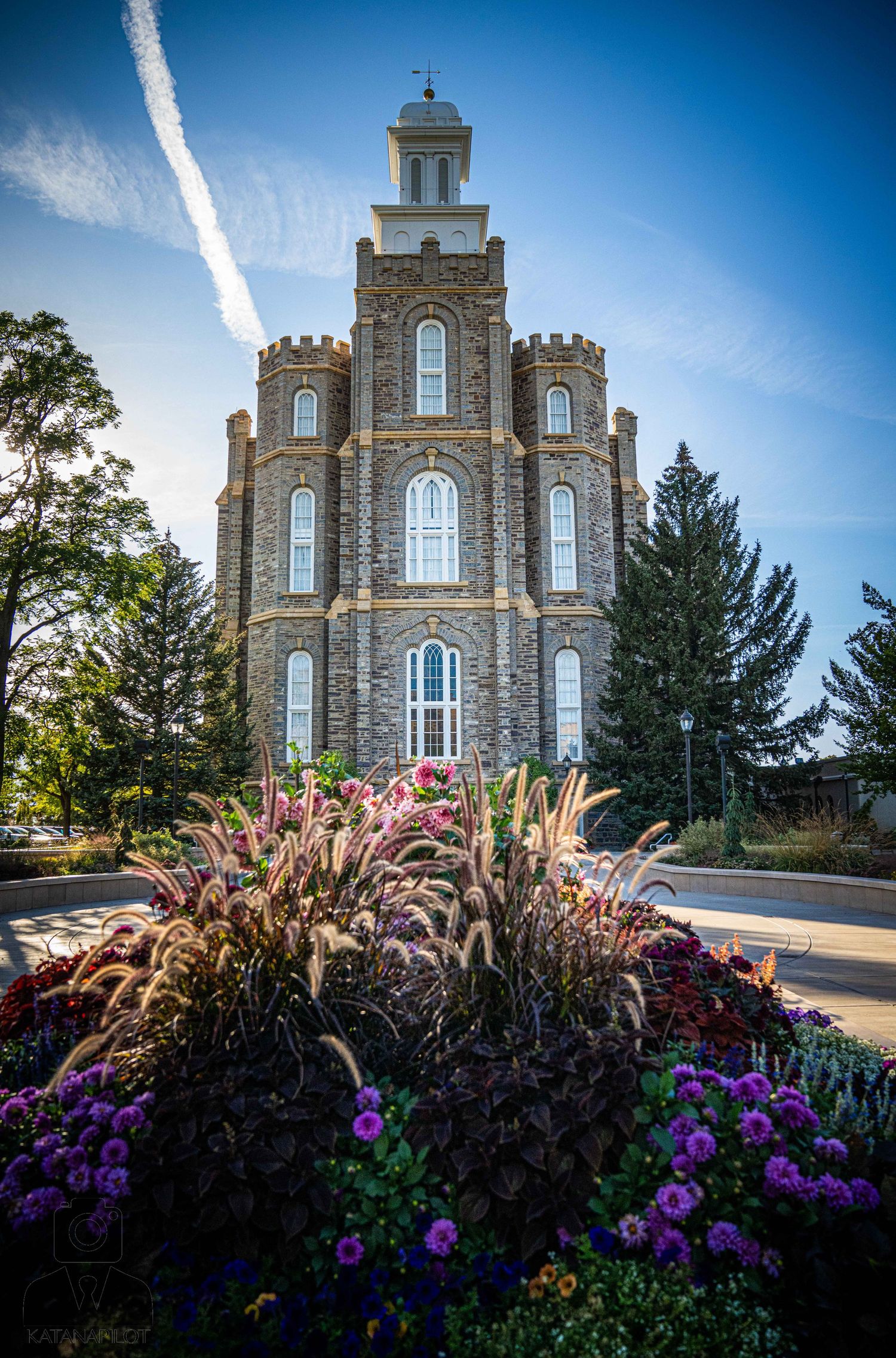 Historic stone temple surrounded by vibrant purple and pink flower gardens in summer.