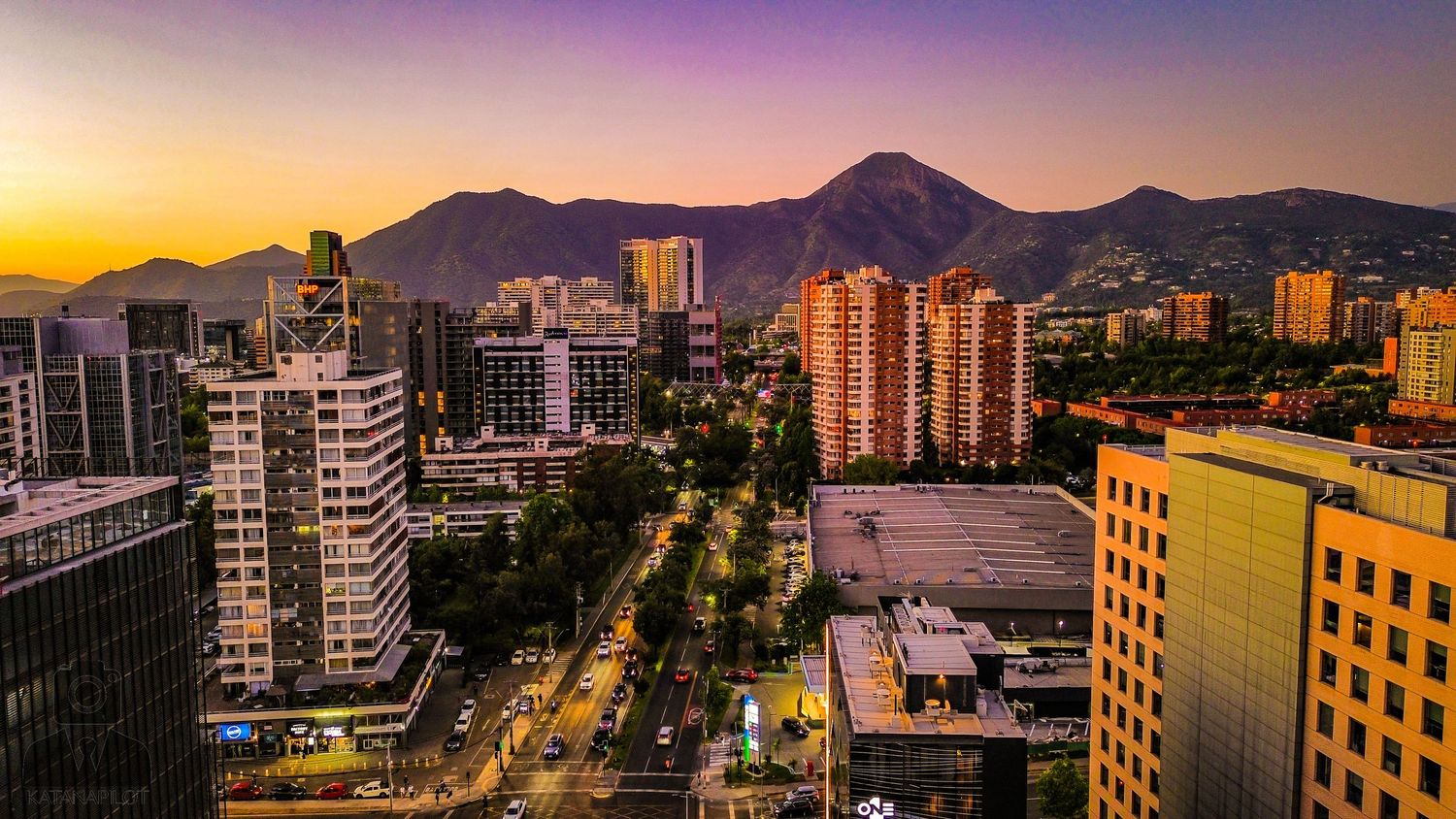 City buildings and mountains under vibrant purple and orange sunset sky.