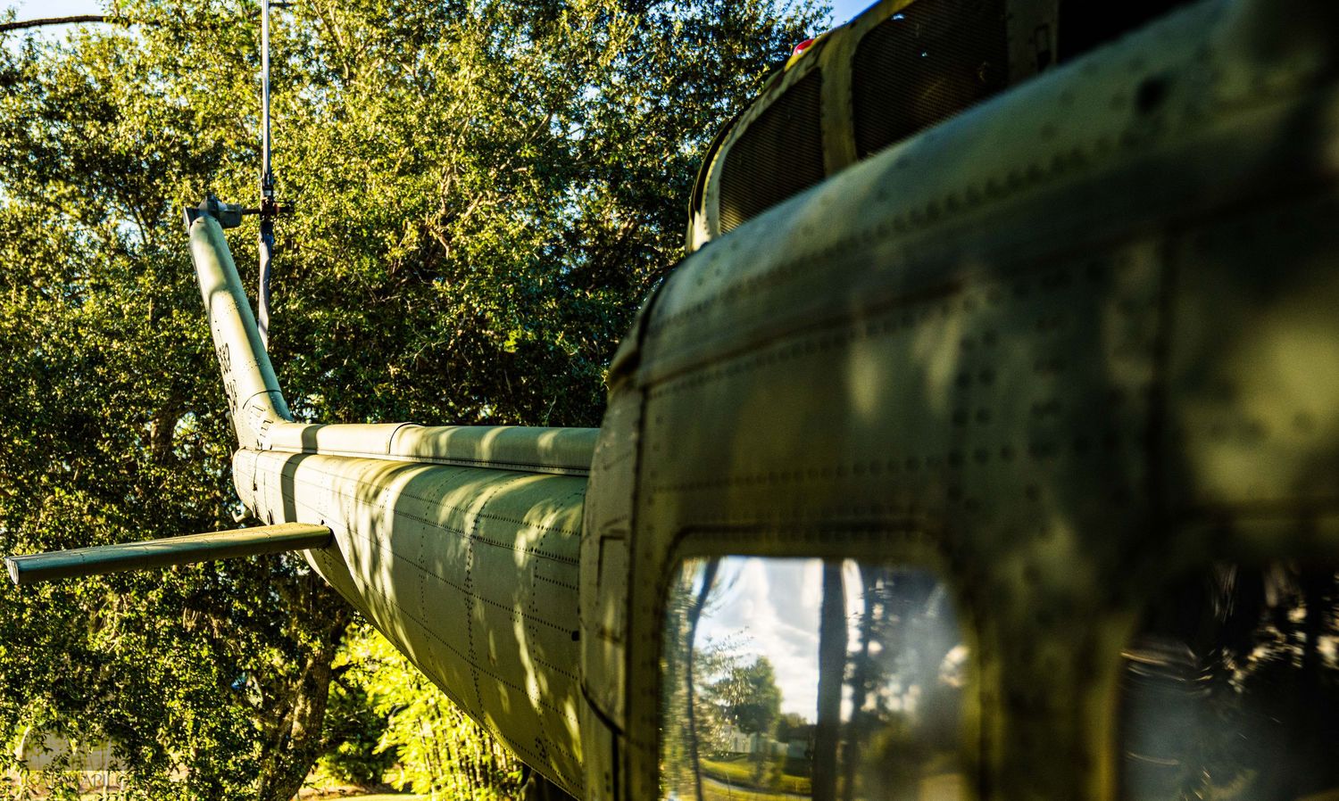 Side view of military helicopter fuselage with trees visible in background.