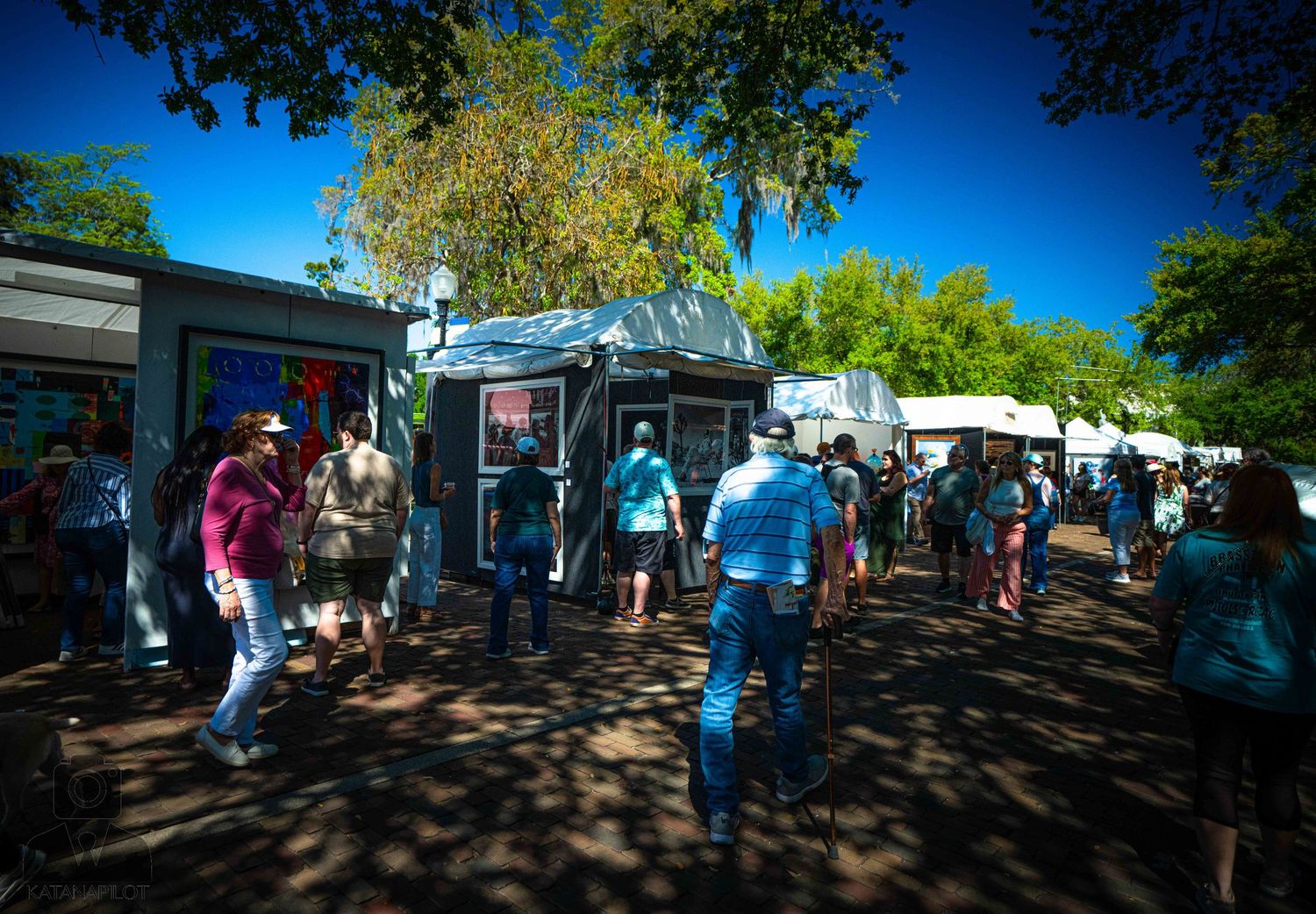People walking along a shaded path on a sunny day with blue sky visible through tree branches.