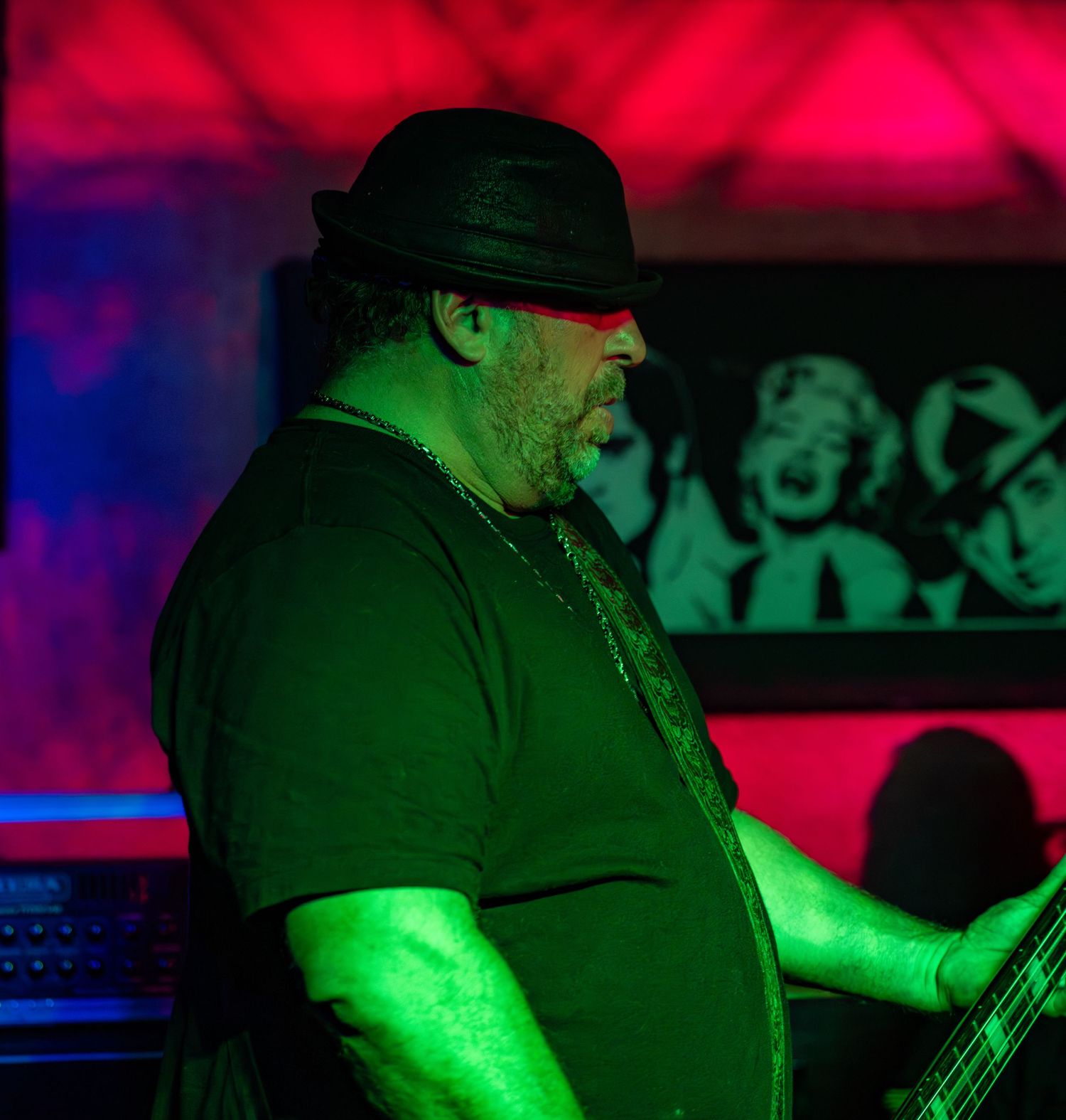 Musician in dark clothing performs under alternating red and green stage lights.