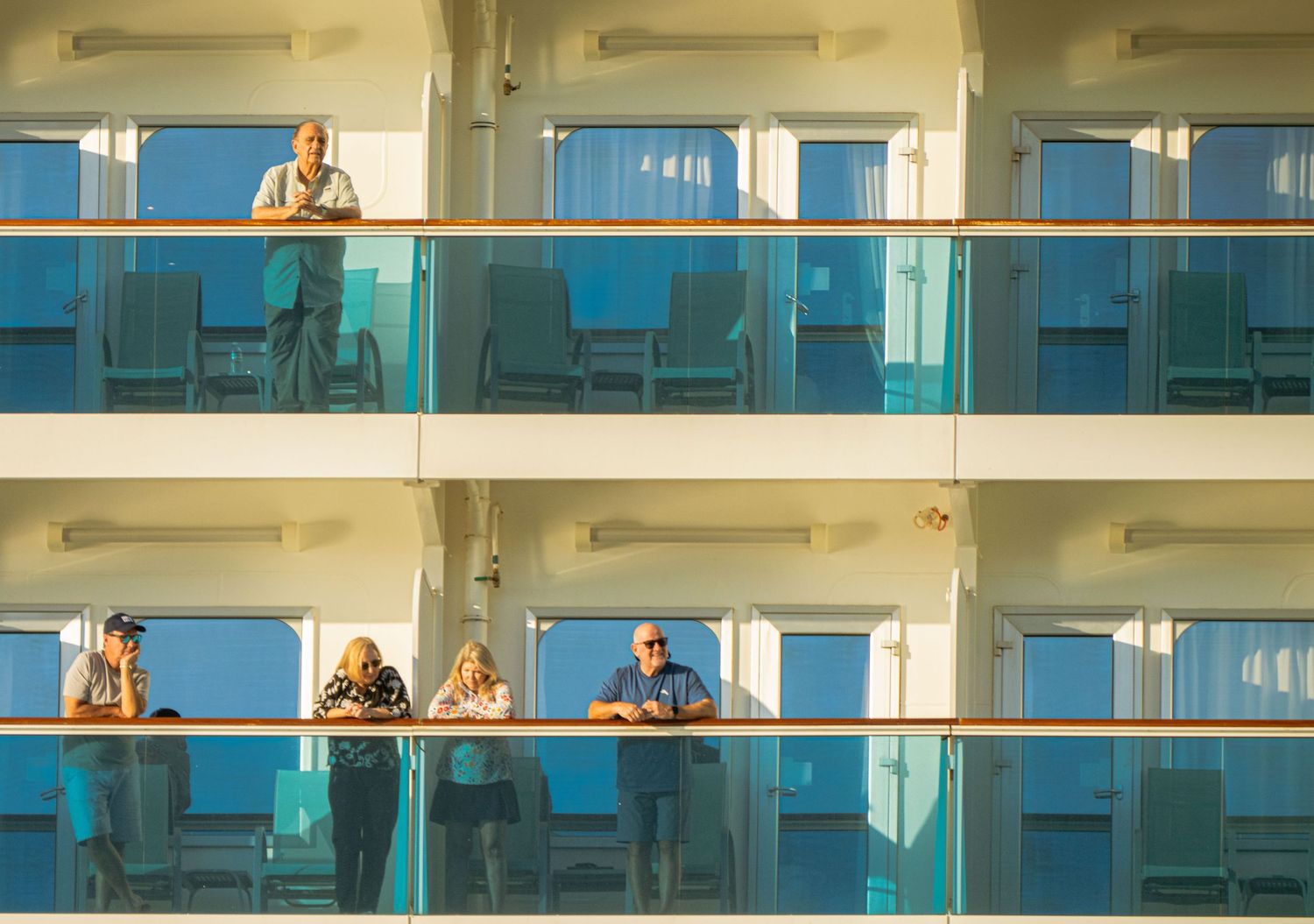People sitting on balconies of a modern glass apartment building during daytime.