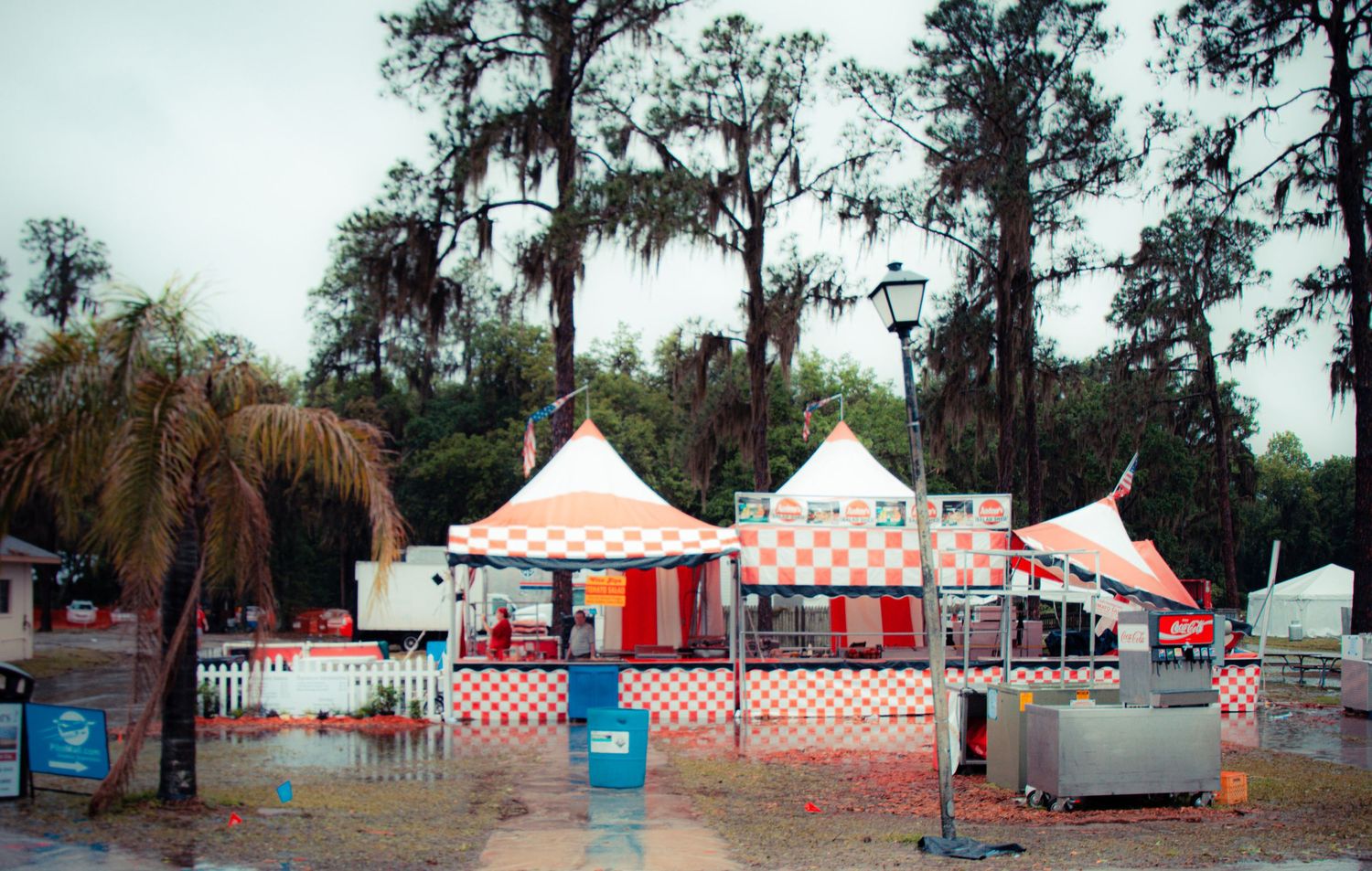 A panoramic view of a carnival setup with red and white striped tents and palm trees in the background.
