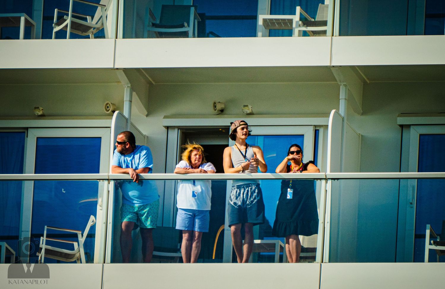 Group enjoying the view from their cruise ship balcony with blue glass windows in background.