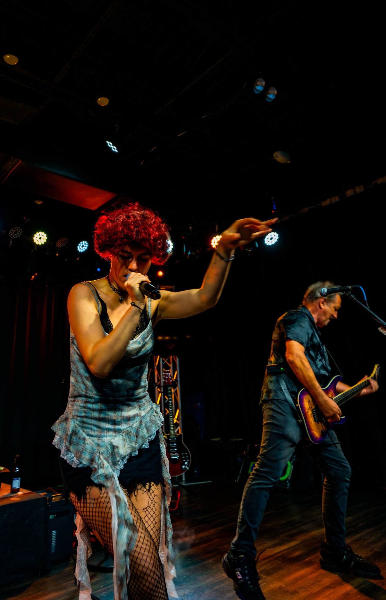 Female singer with red curly hair performs on stage in fishnet stockings while guitarist plays behind her.