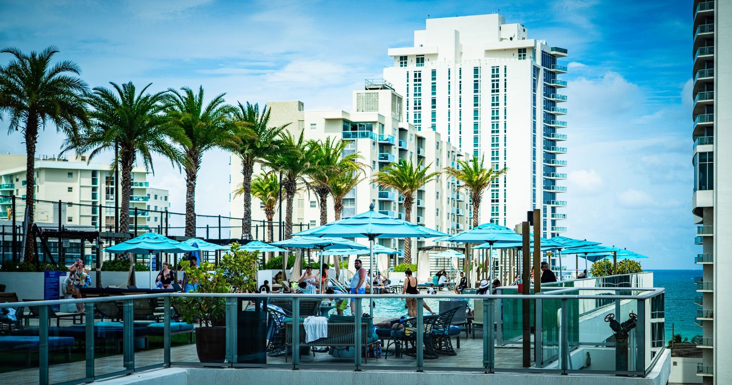 Panoramic view of modern waterfront buildings and palm trees along an urban boardwalk.