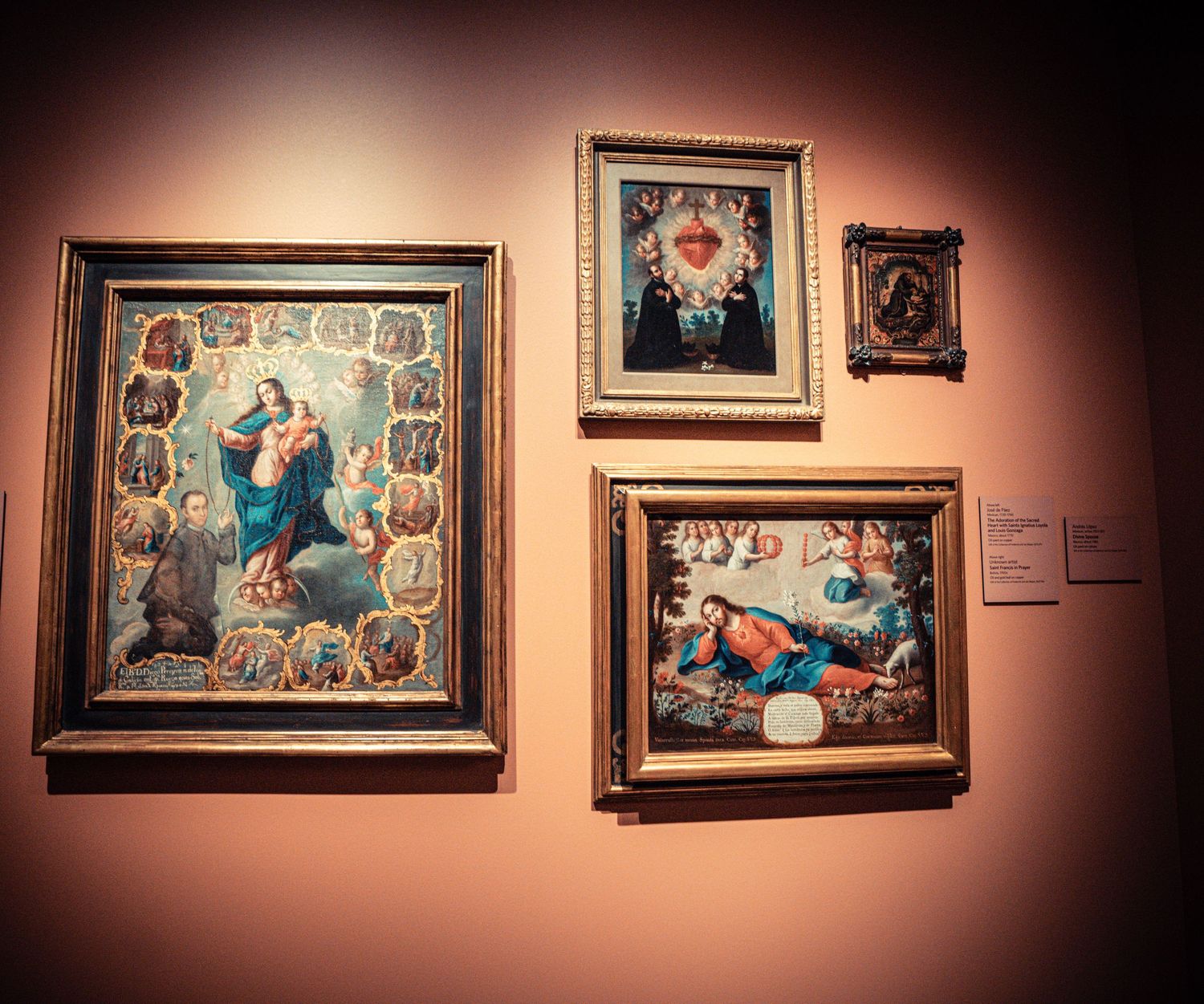 Art gallery wall displaying multiple framed paintings with dramatic lighting against a dark burgundy background.