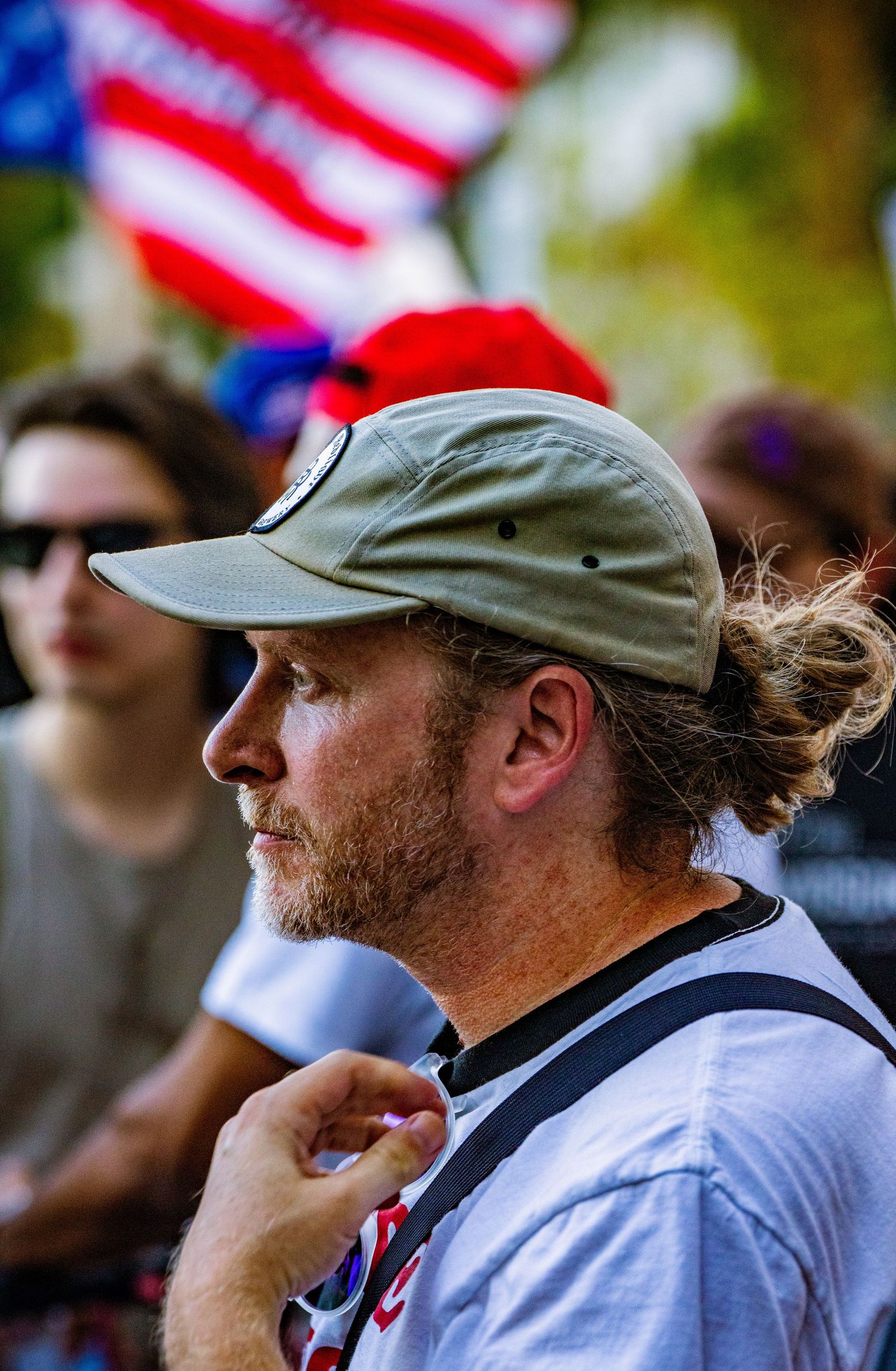 A spectator in a gray baseball cap watches an event with American flags visible in the background.