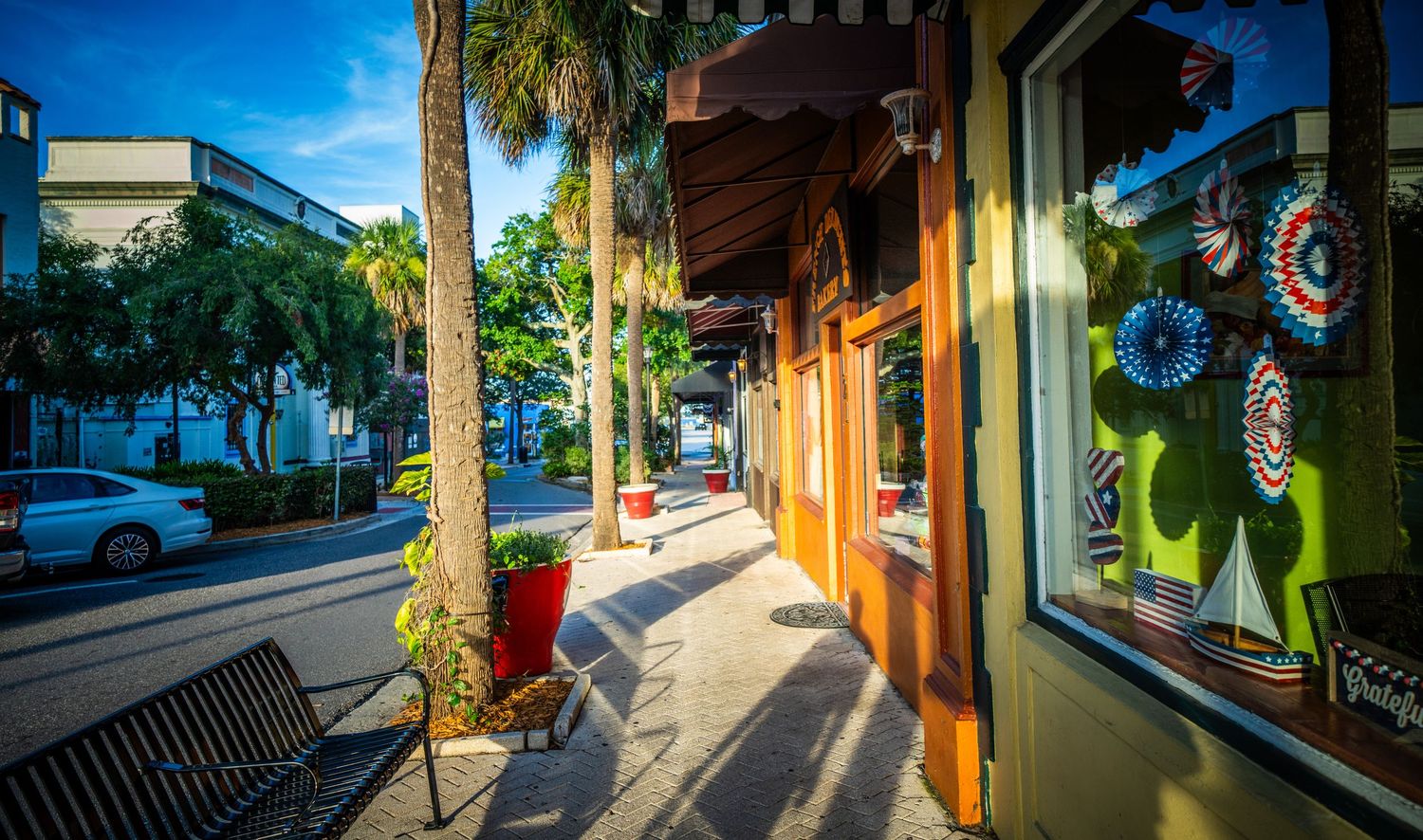 Palm trees and storefronts casting shadows along a sunny commercial street.