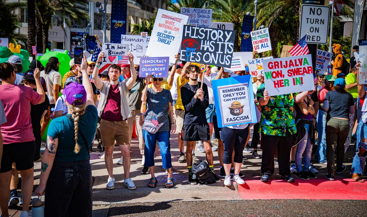 Crowd of protesters holding signs and banners during daytime demonstration in urban setting.