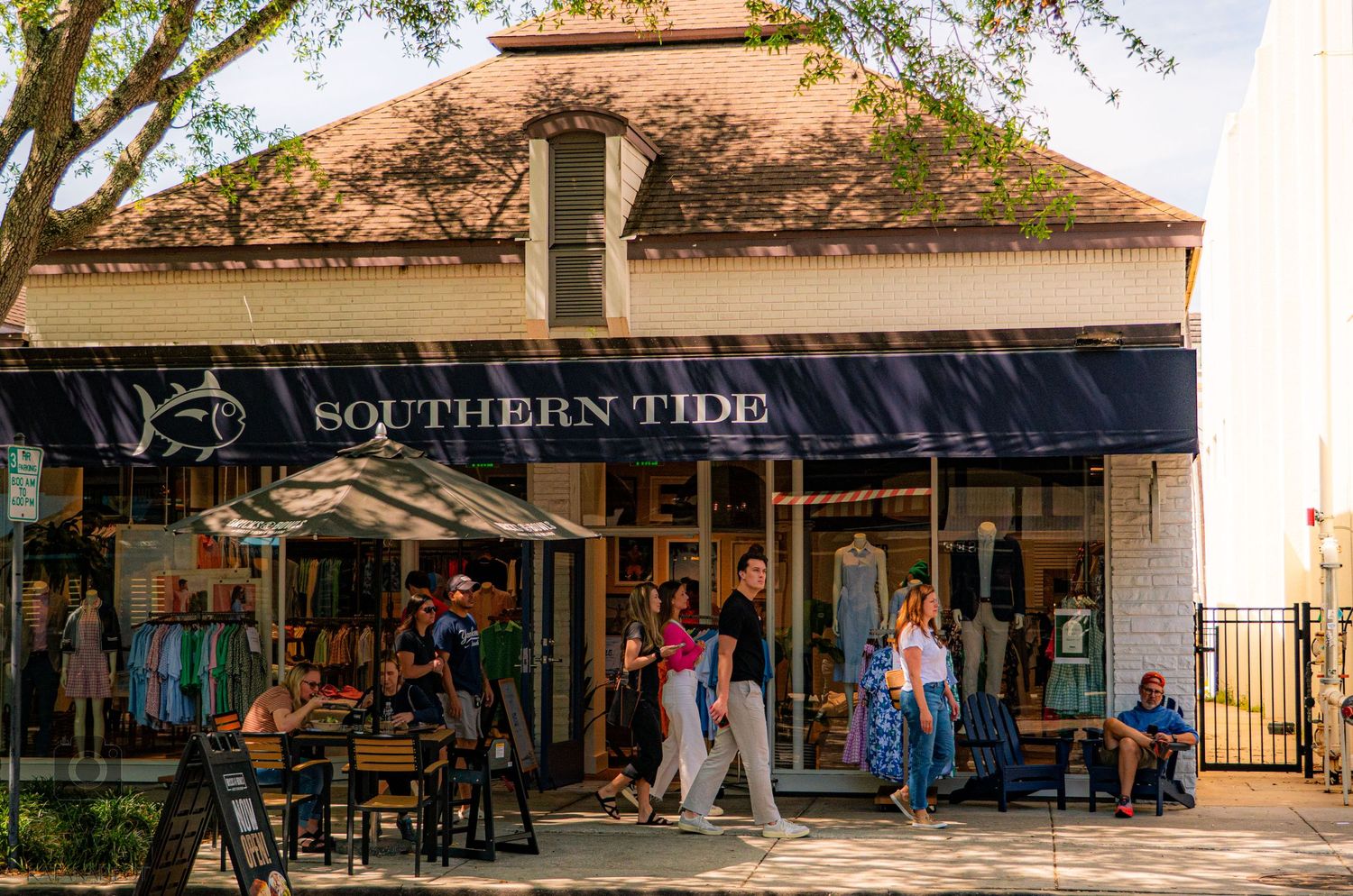 Row of retail storefronts with awnings and pedestrians walking along a shopping district.