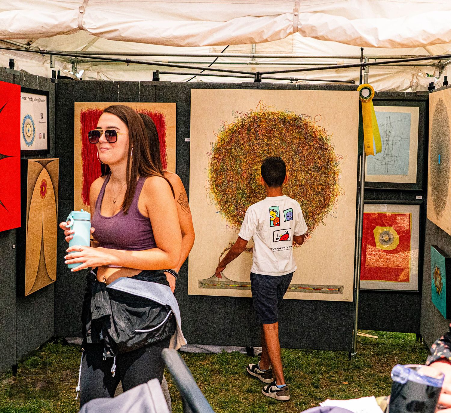 Art fair tent displaying various artworks and prints with visitors browsing the collection.