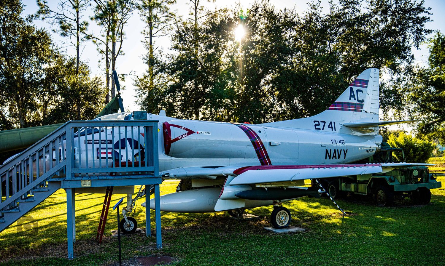 Row of vintage military planes parked on grass under bright sunlight and trees.