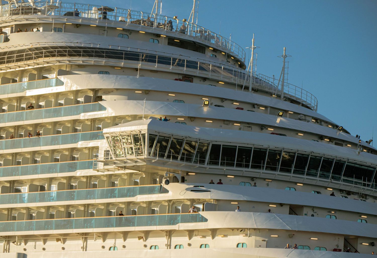 A luxury cruise ship's exterior showing multiple decks and balconies against a bright blue sky.