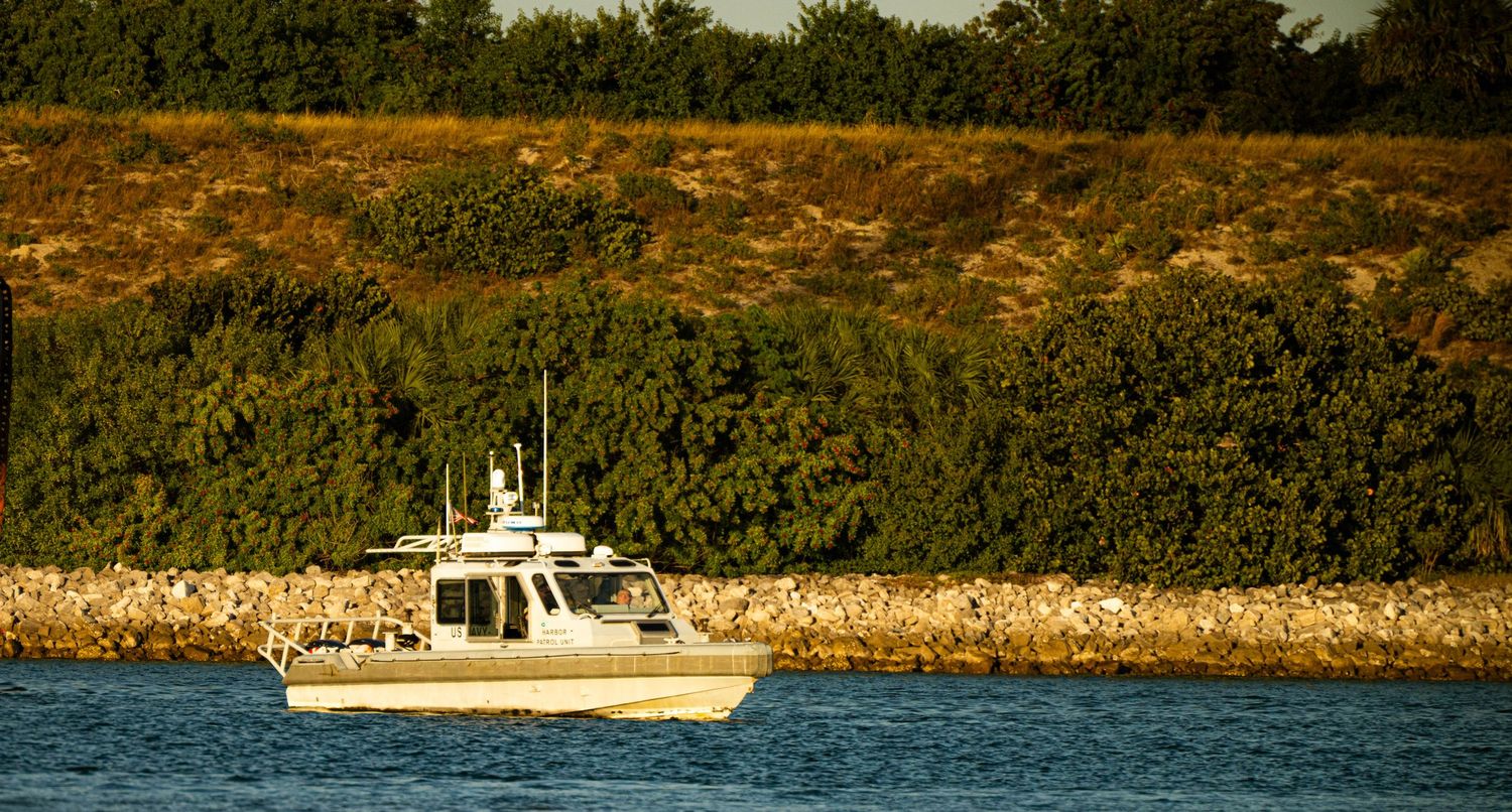 Boats navigate along a scenic shoreline with rocky cliffs and dense vegetation on a sunny day.