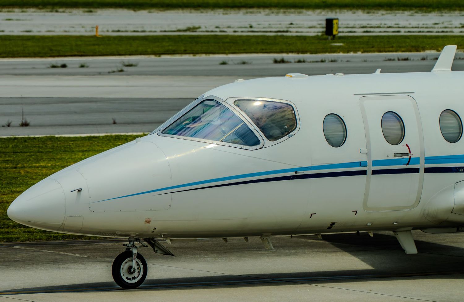 Close-up of a white private jet with blue trim on airport tarmac, showcasing cockpit and oval windows.