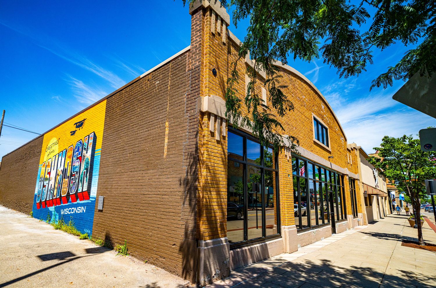 Corner brick building with modern windows and colorful mural on its side wall.