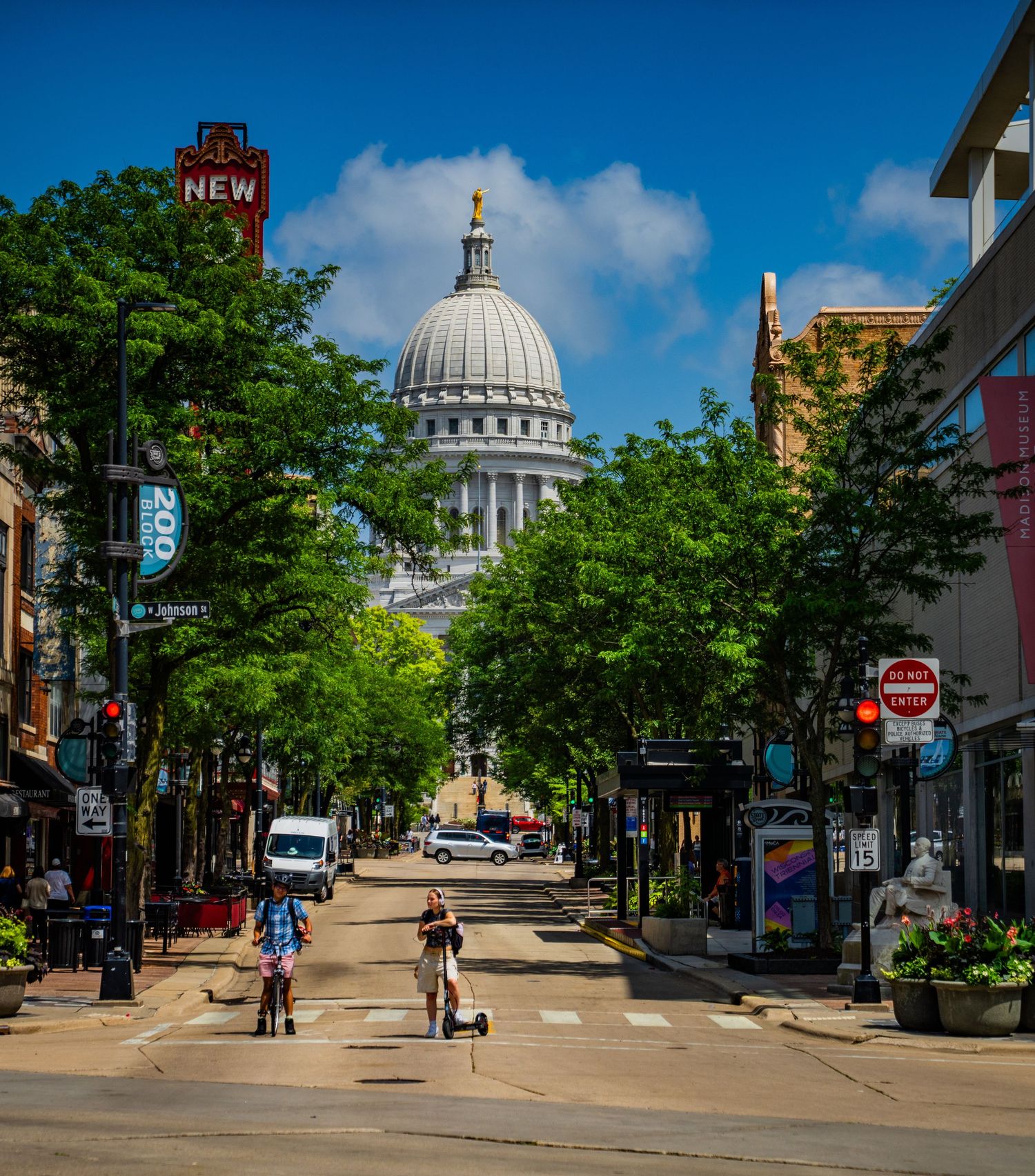 Tree-lined city street leads to a domed government building visible in the distance.