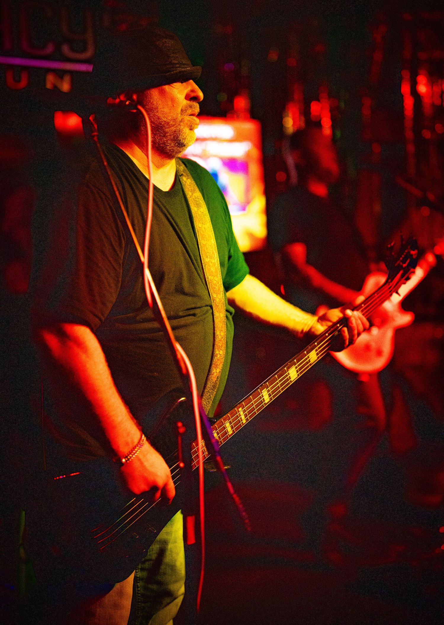Bass guitarist performs on stage illuminated by dramatic red stage lighting.