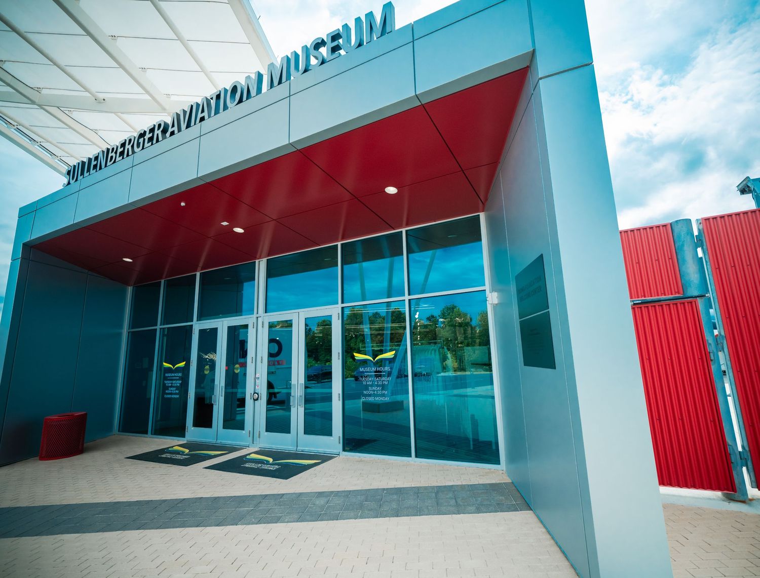 Modern museum exterior featuring clean lines and glass windows with turquoise and red architectural elements.