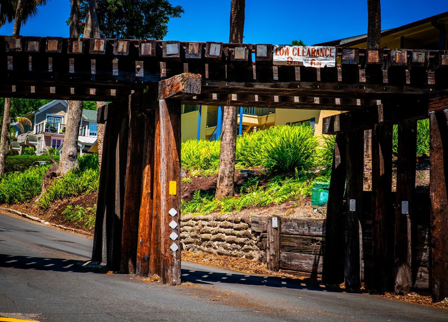 Rustic wooden fence walkway under bright blue sky with trees casting shadows.