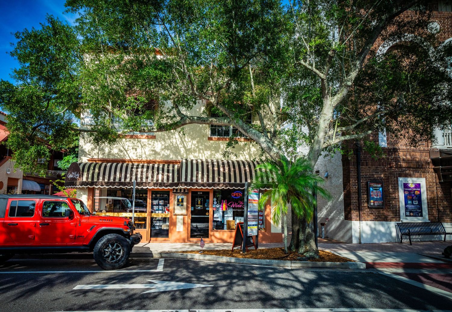 Charming storefront with striped awning and red truck parked on tree-lined street.