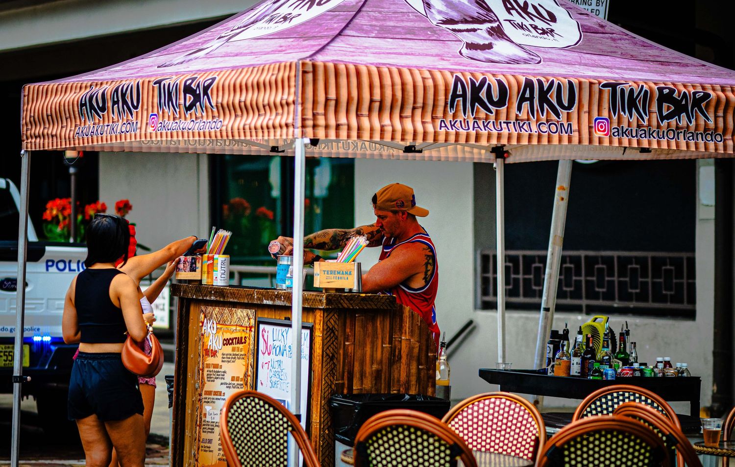 Customer ordering at Aku Aku Tiki Bar outdoor booth with colorful striped canopy at a sunny event.