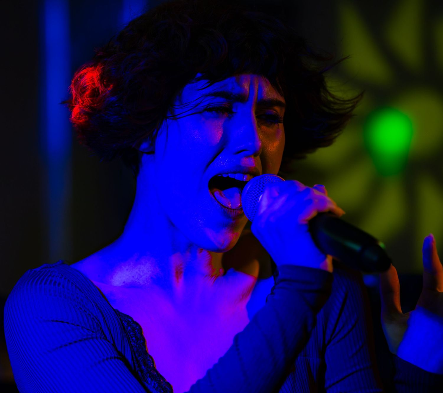 Concert performer illuminated by vibrant blue stage lighting while singing into a microphone.