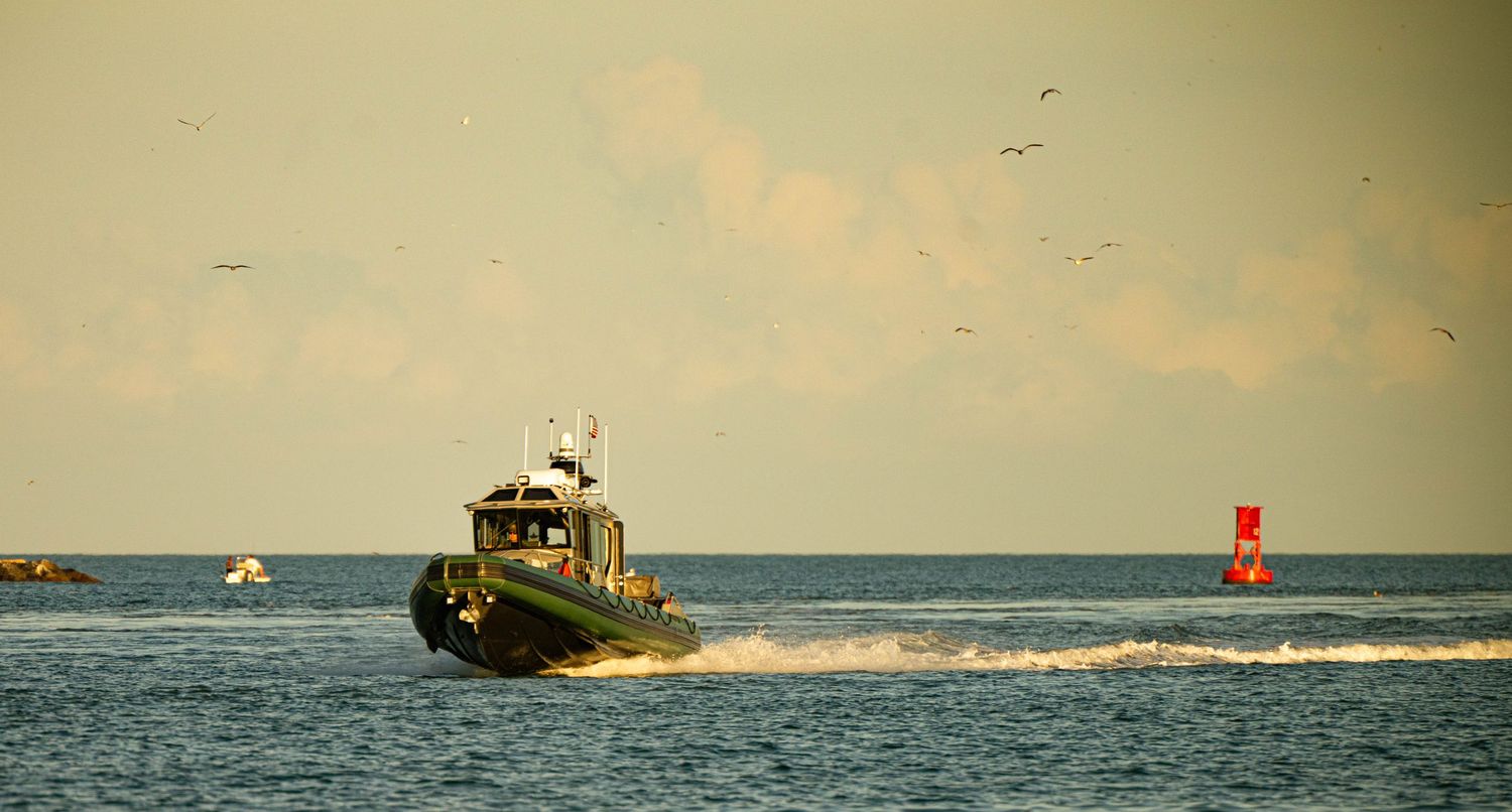 A series of small boats navigate choppy ocean waters near buoys during an overcast day.