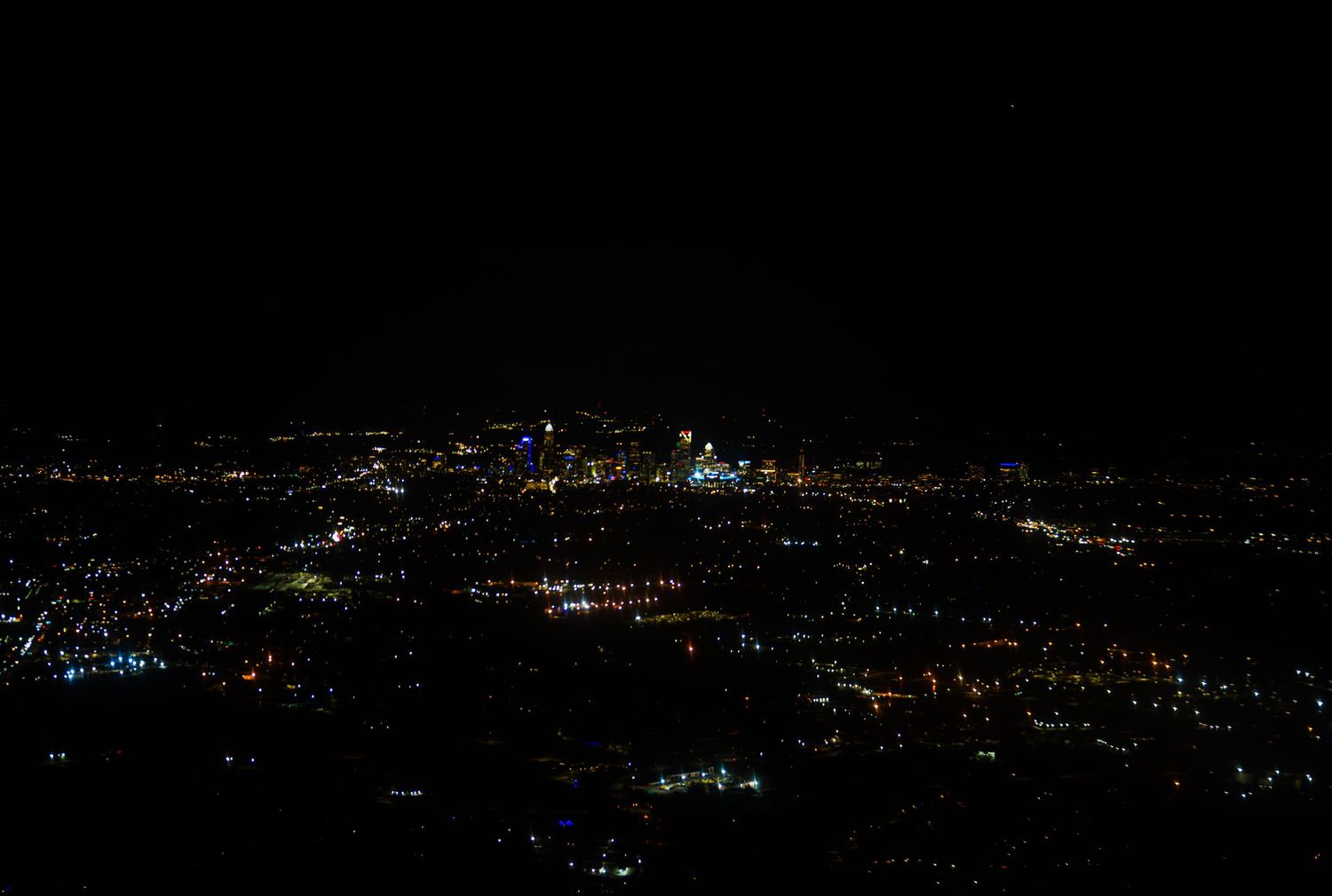 Panoramic nighttime view of city lights stretching across a dark hillside with twinkling illumination in the distance.