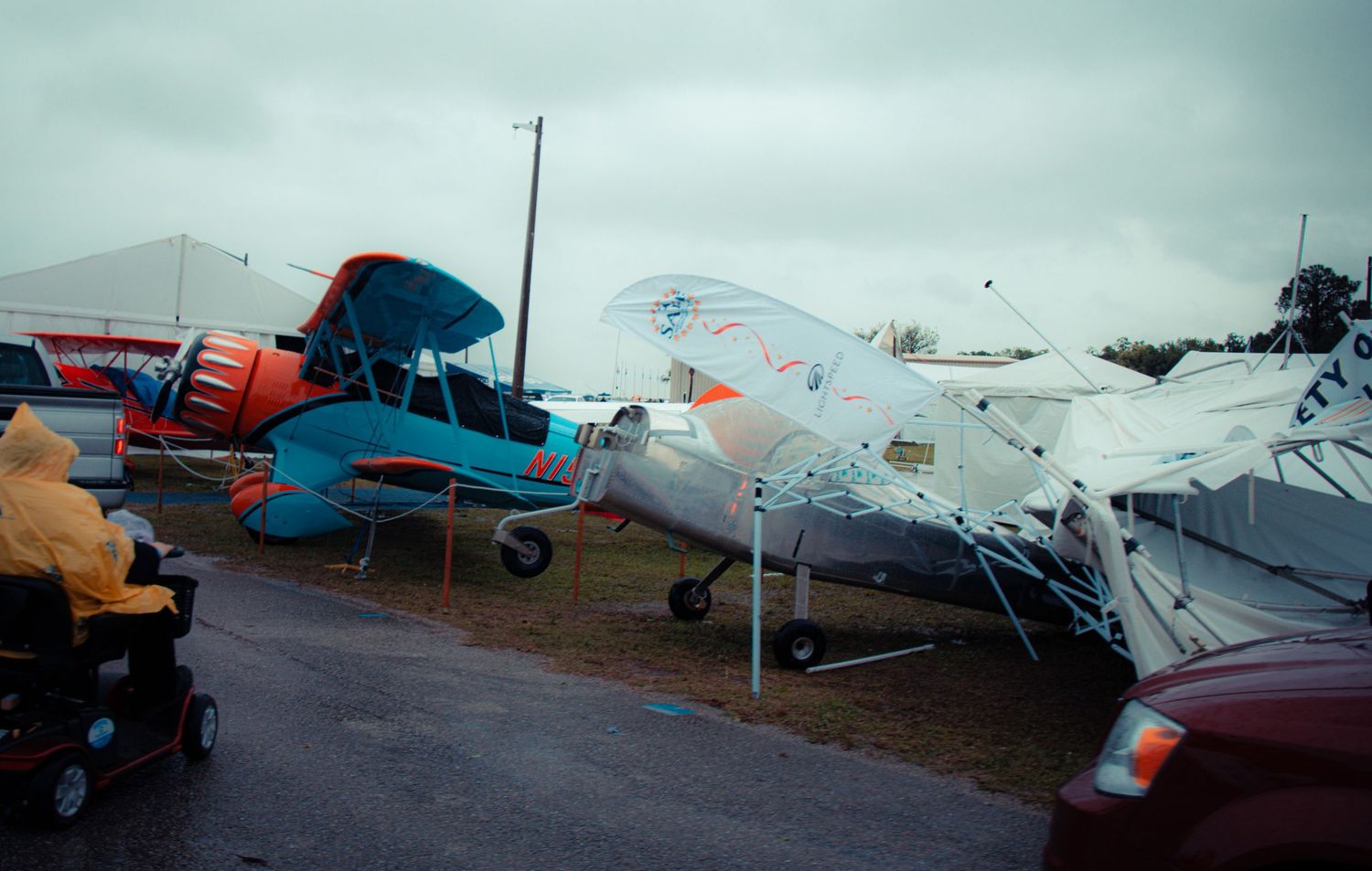 A row of small aircraft parked on an airfield with blue and orange colored planes visible in the panoramic view.