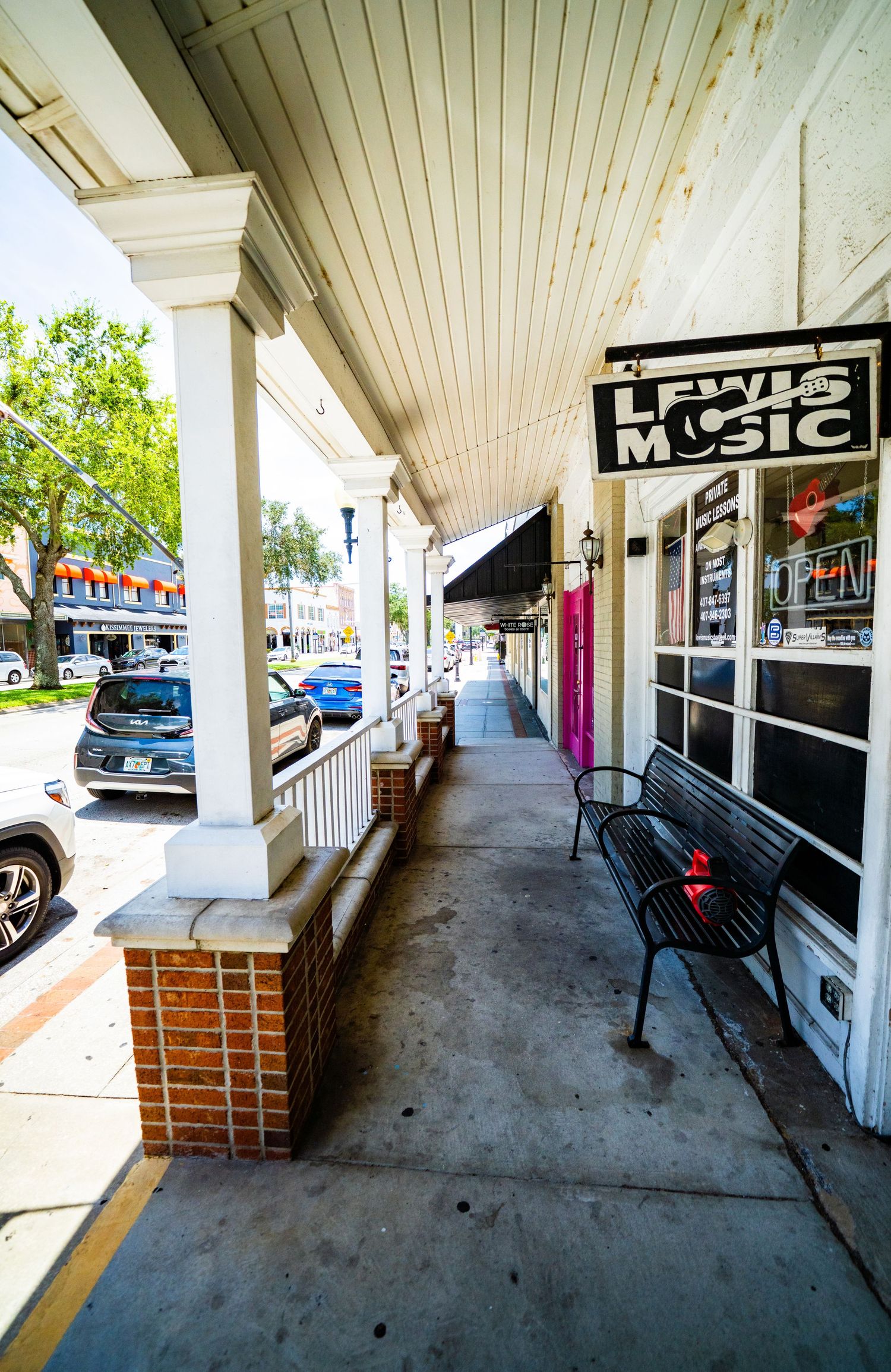 Covered walkway with benches along downtown storefronts showing music shop signage.