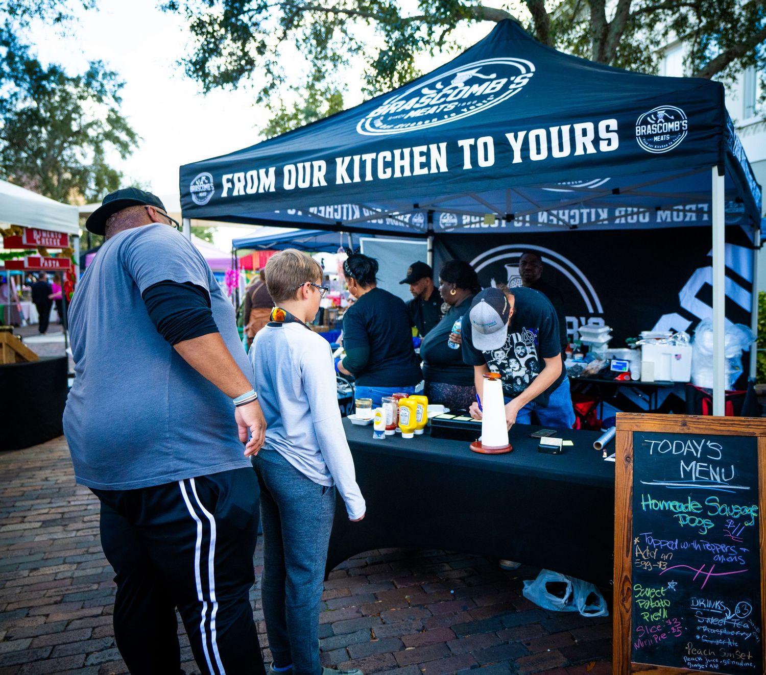 Food truck vendors serve customers at an outdoor event with black canopy tents and menu boards.