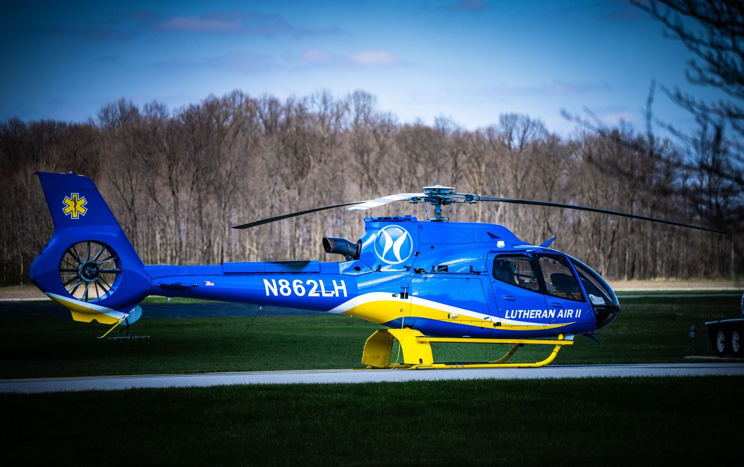 Blue and yellow helicopter parked on landing pad with registration number visible.