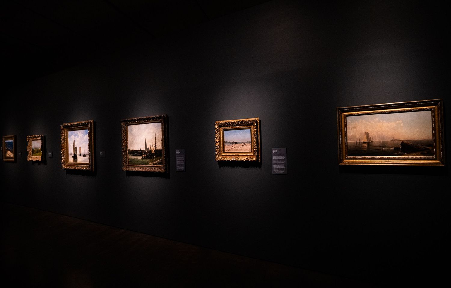Art gallery interior with illuminated paintings on dark walls creates dramatic museum atmosphere.